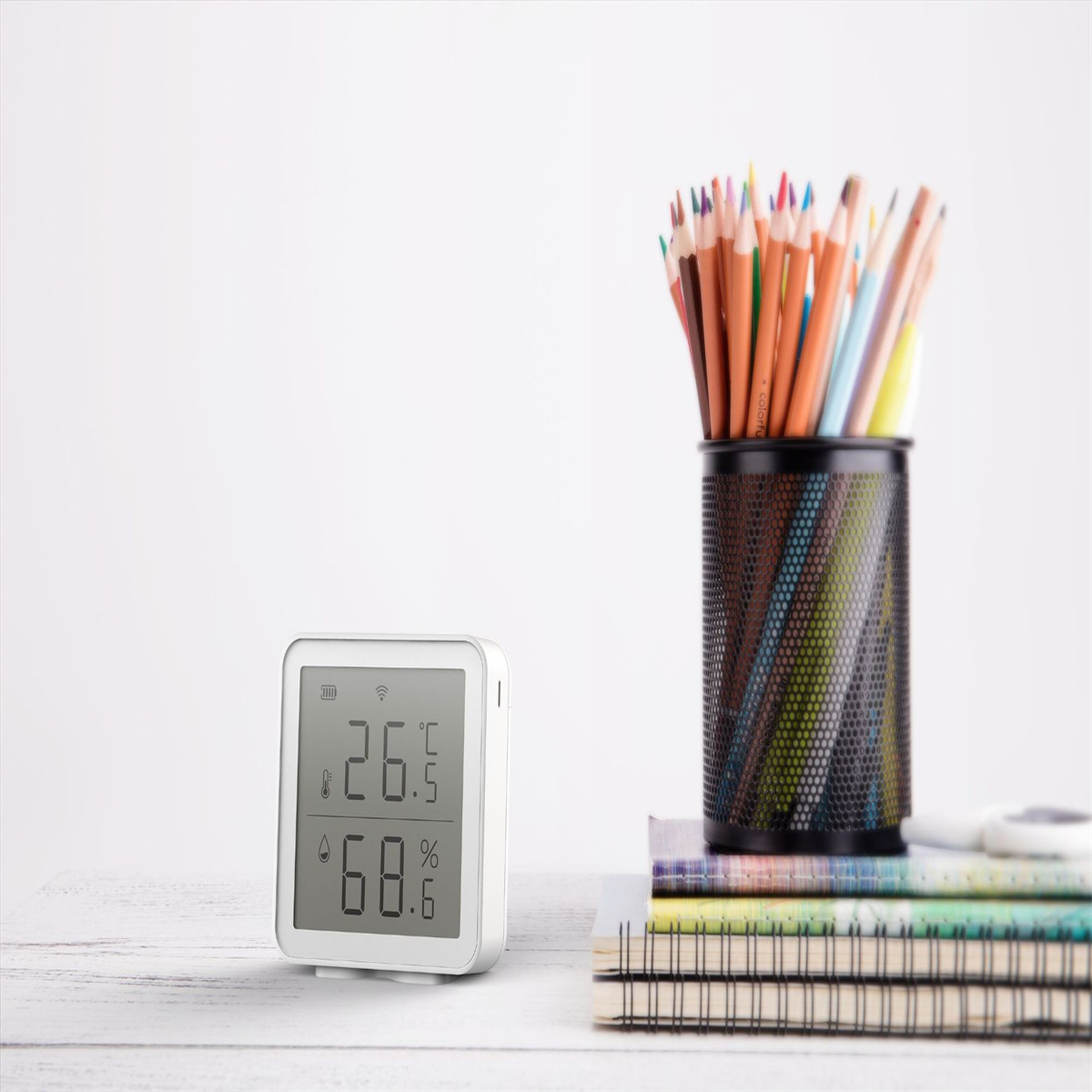 Weißer Schreibtisch mit Thermometer, Bleistiften und Notizbüchern, vor weißem Hintergrund.