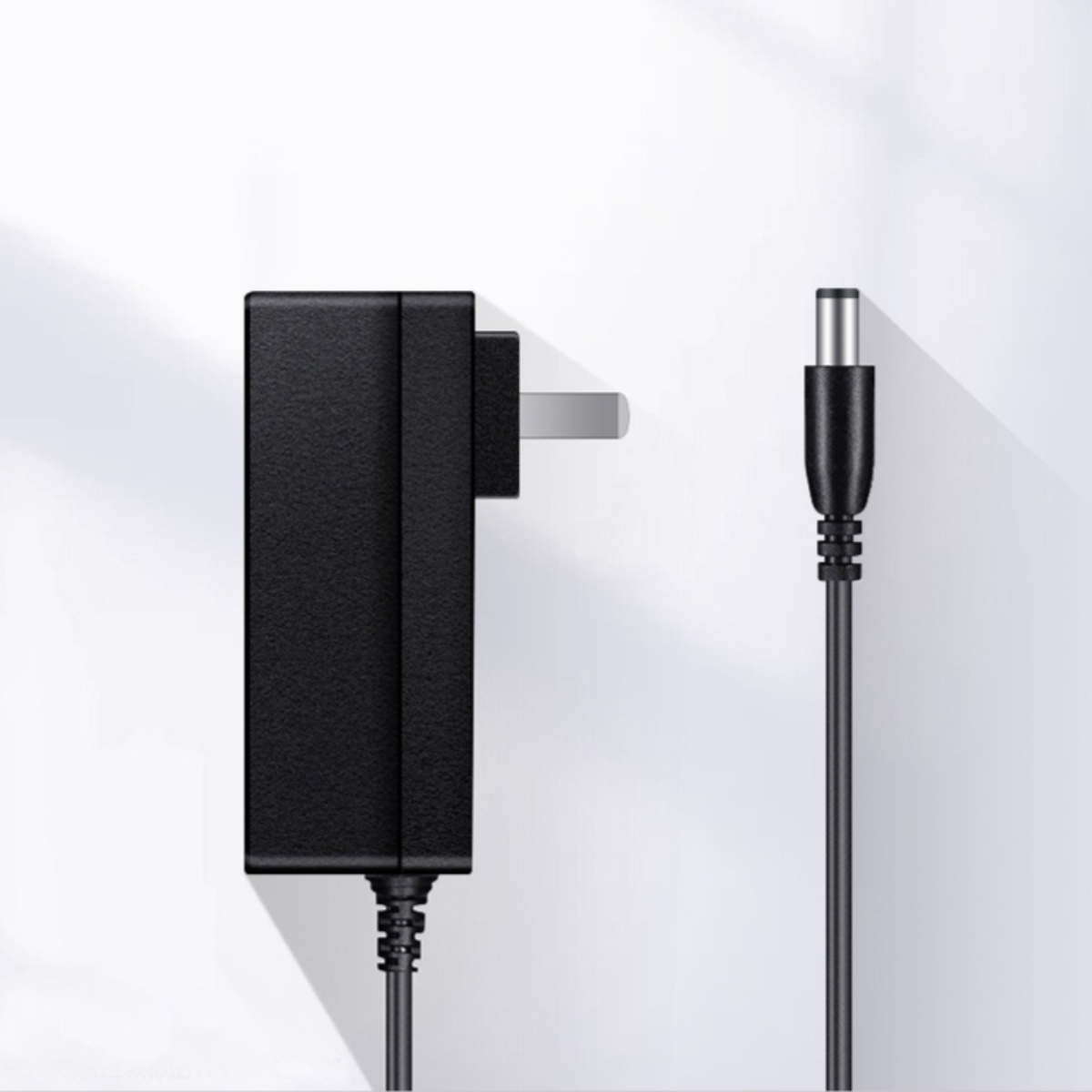 Schwarzes Netzteil mit Stecker und Kabel auf Weiß. Kabel rechts.