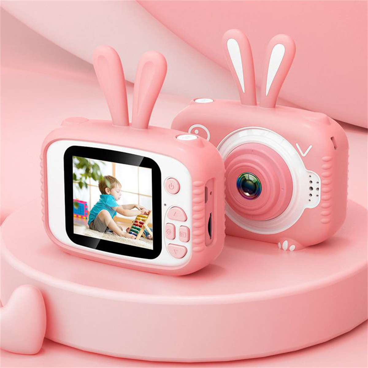 Zwei rosa Spielzeugkameras mit Hasenohren auf einer rosa Plattform, mit einem Kinderfoto auf einem Bildschirm.