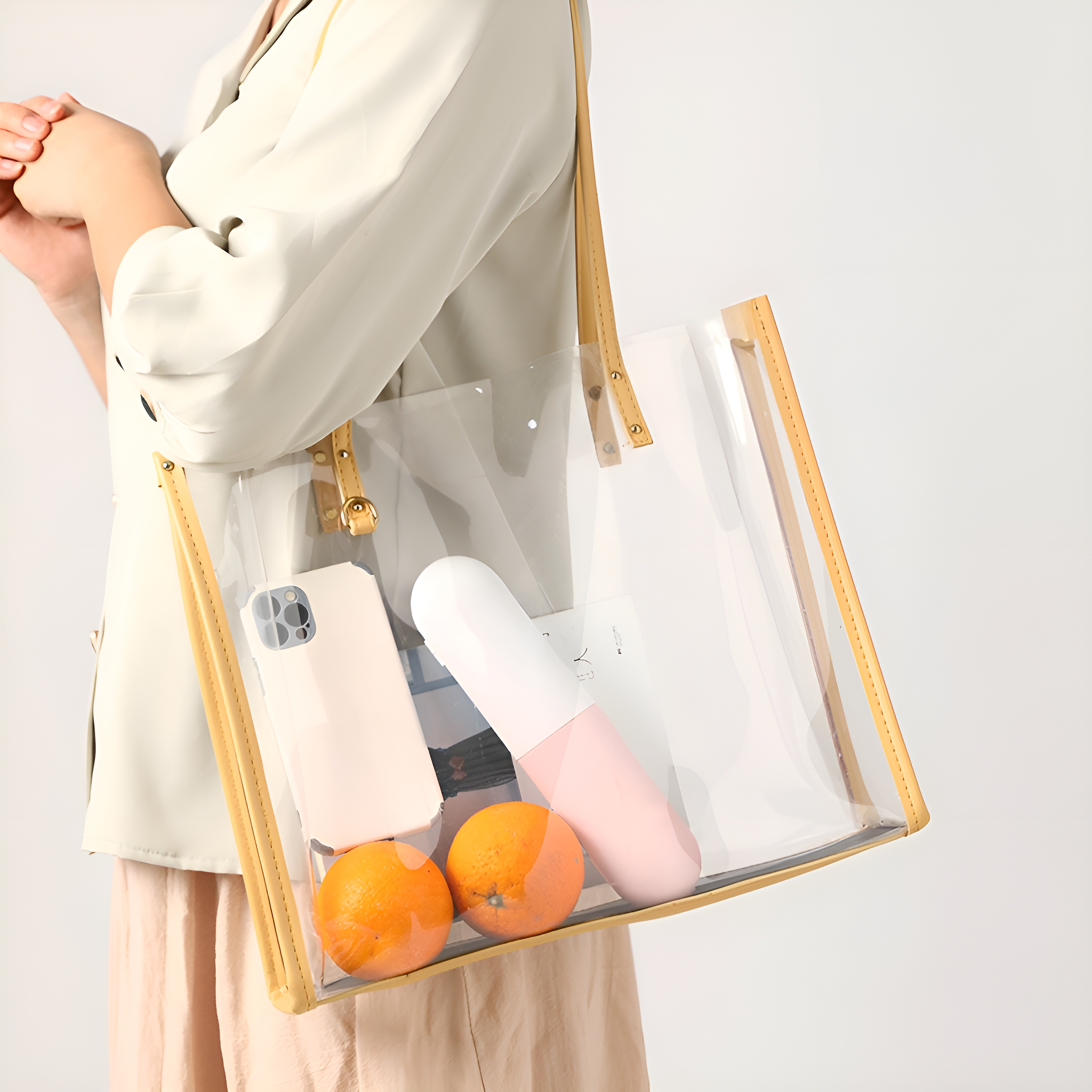 Eine Frau hält eine transparente Tragetasche mit Orangen, einem Telefon und einem rosa Objekt. Die Tasche hat braune Verzierungen.