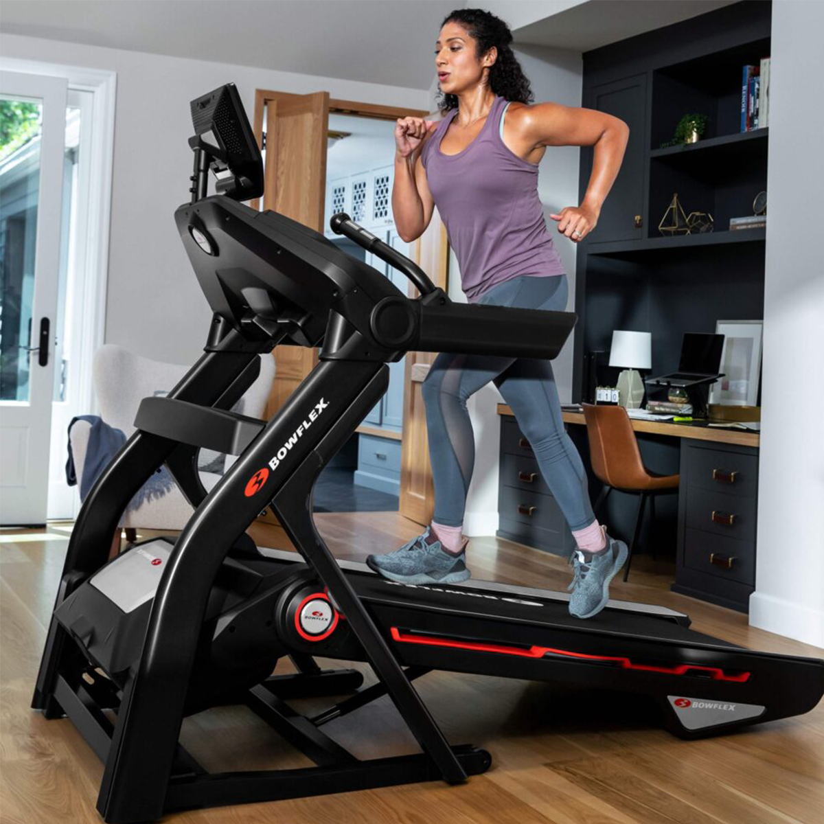 Femme courant sur un tapis roulant noir dans une salle de sport à domicile. Bureau en arrière-plan.