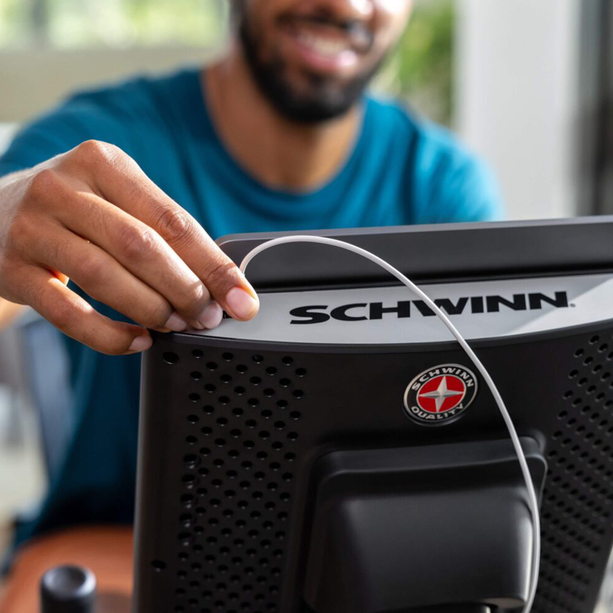 Ein Mann verbindet ein weißes Kabel mit einem schwarzen Schwinn-Heimtrainer-Display.