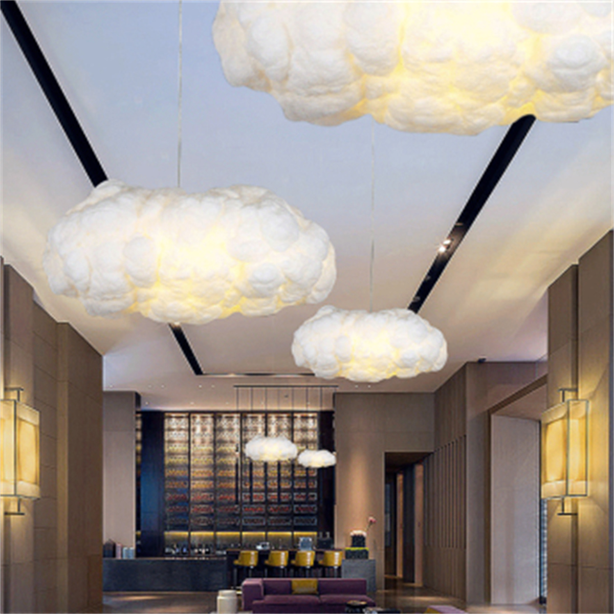 Wolkenförmige Lichter hängen an einer Decke in einem modernen Innenraum mit Bar und Sitzbereich.
