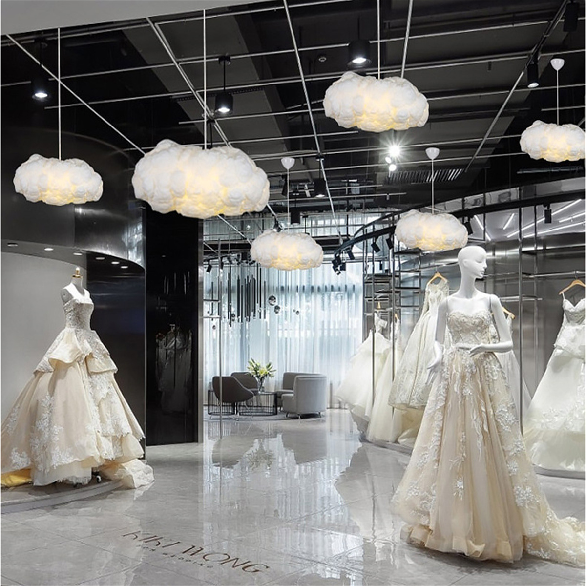 Brautkleider in einem Geschäft. Wolkenförmige Lichter hängen von der Decke.