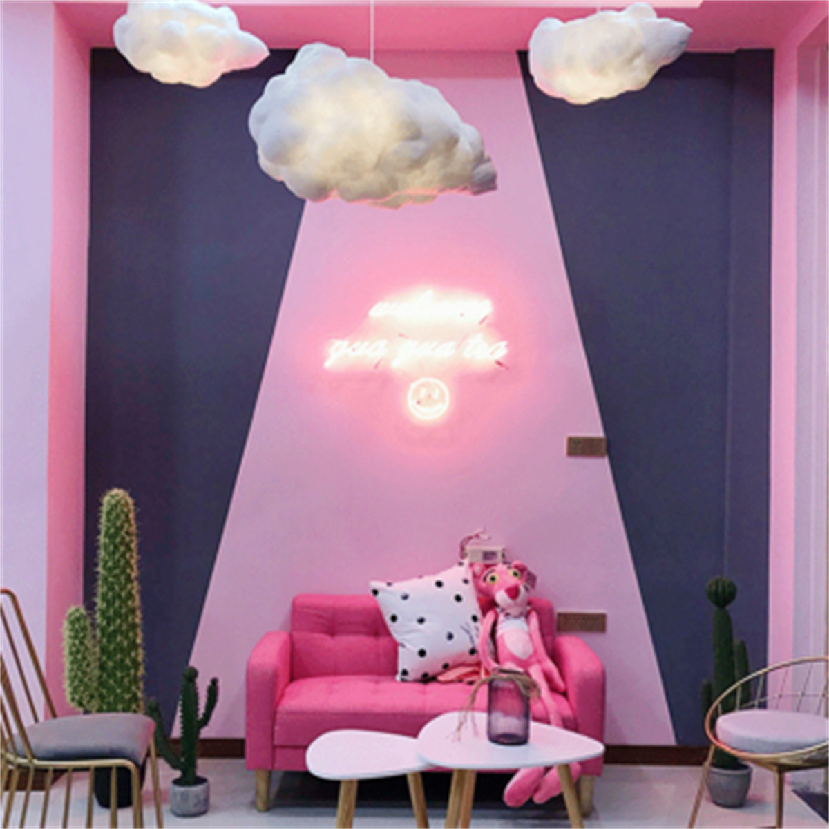 Ein pinkfarbener Raum mit Wolkenlichtern, einem pinkfarbenen Sofa und einem Neon-Schild mit 'you are magic'.