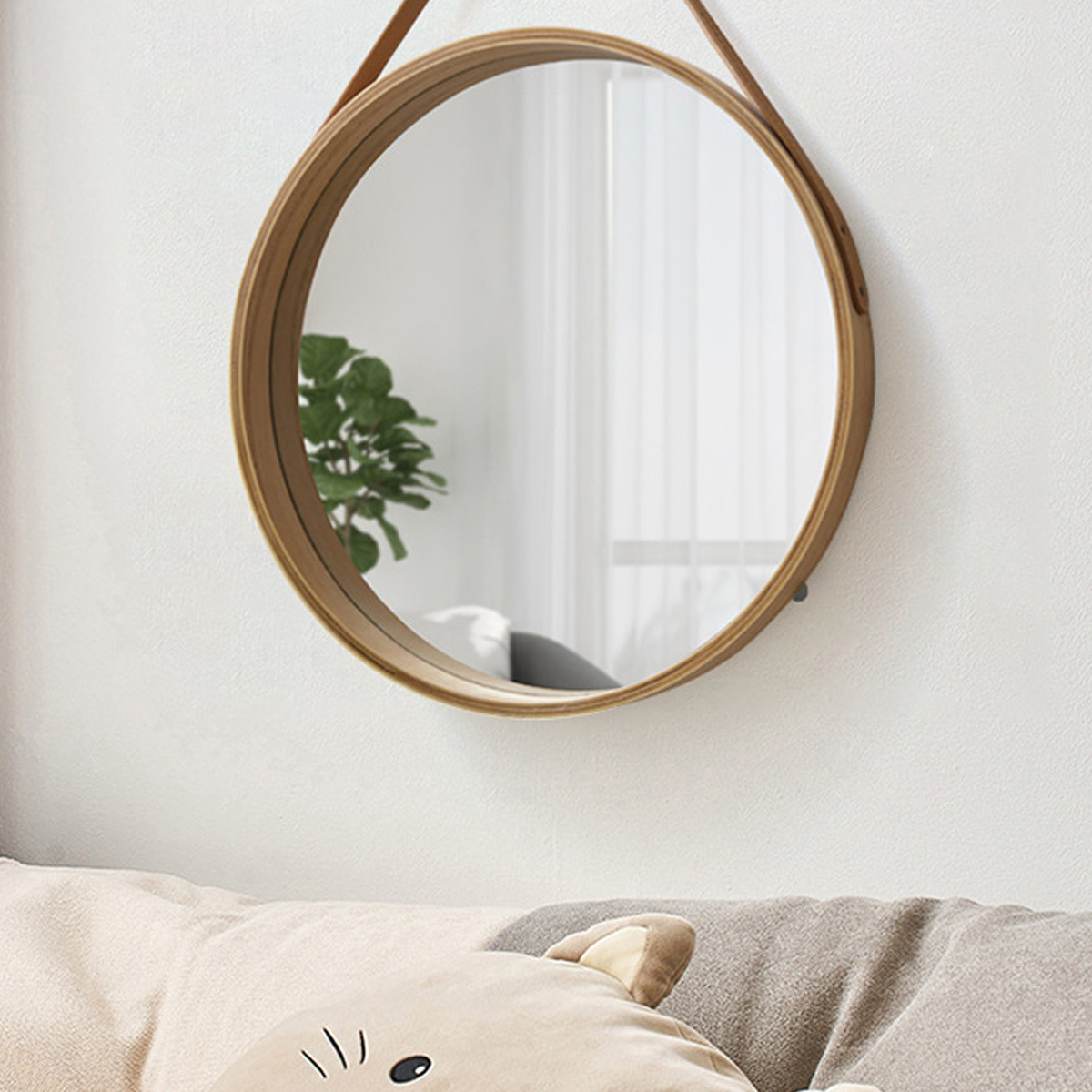 Runder Spiegel mit Holzrahmen, hängt an weißer Wand. Sofa und Kissen im Spiegelbild.