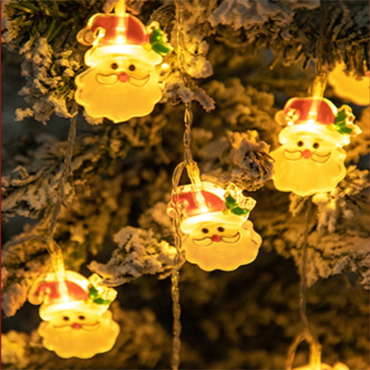 Weihnachtsbeleuchtung mit Santa-Gesichtern, die an einem Baum mit Schnee hängen.