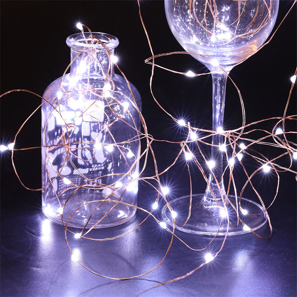 Klare Glasflaschen und ein Weinglas mit weißen LED-Leuchten. Dunkler Hintergrund.