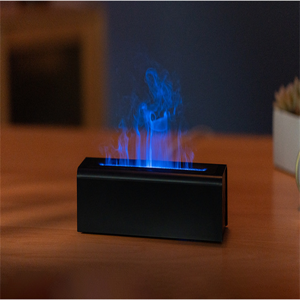 Schwarzes rechteckiges Gerät, das blaue, simulierte Flamme emittiert. Es steht auf einem Holztisch.