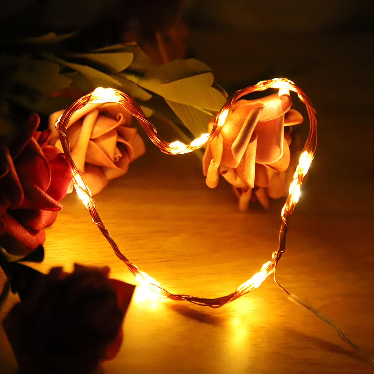 Ein herzförmiger Lichterkettenstrang mit Blumen im Hintergrund.