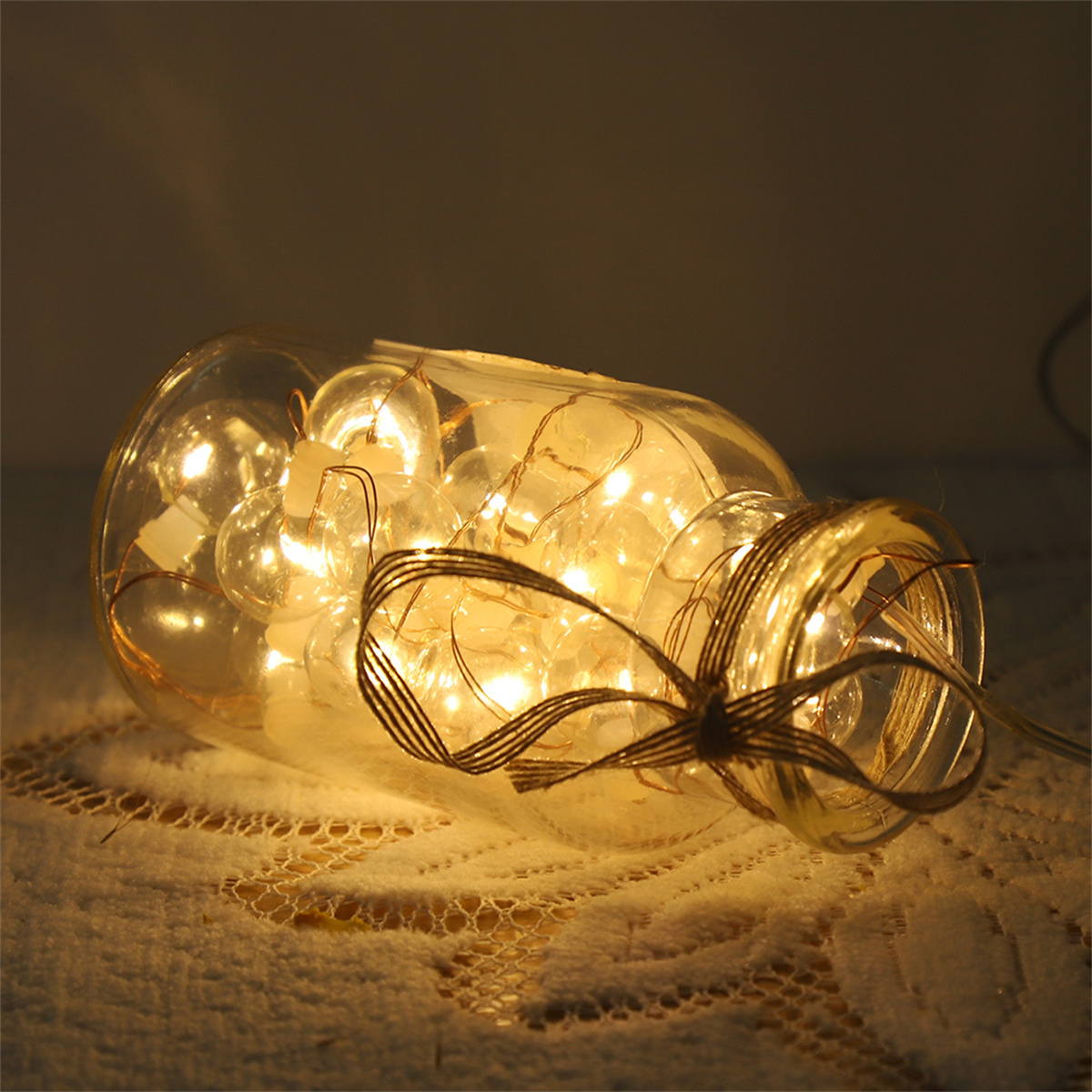 Glasflasche mit Lichterketten und braunem Band.