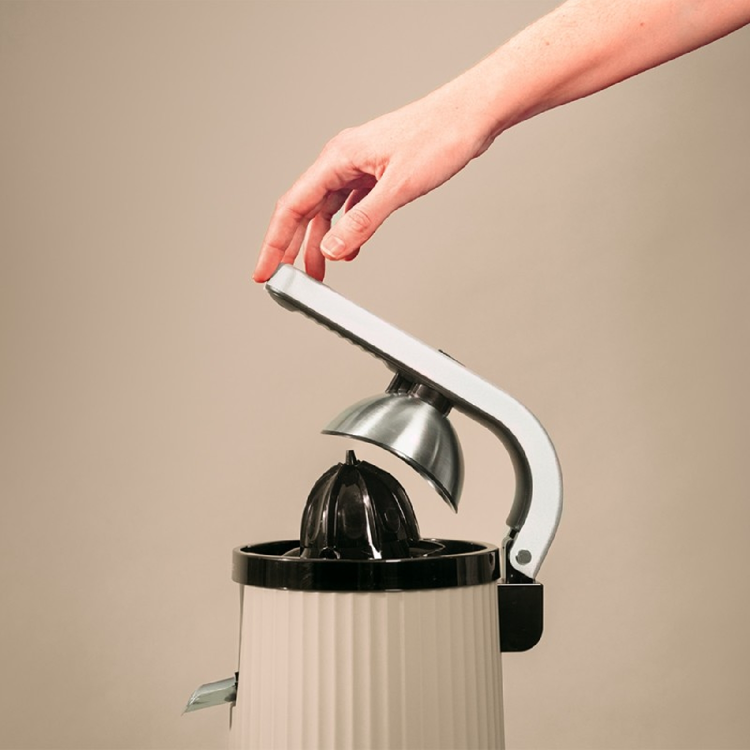 Una mano aziona uno spremiagrumi color crema, con un alesatore nero.