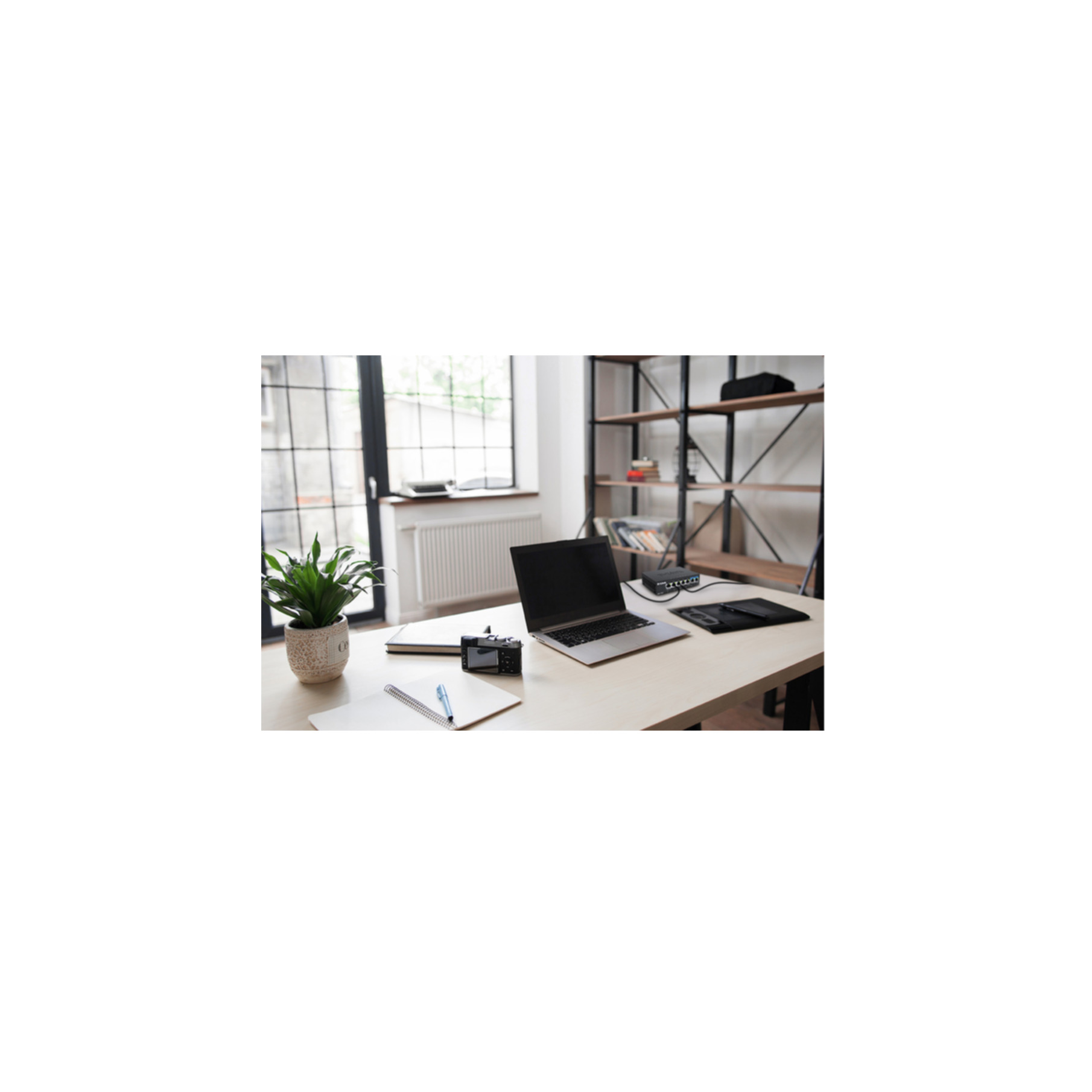 Miejsce pracy z laptopem, aparatem, notatnikiem i rośliną doniczkową przy oknie.