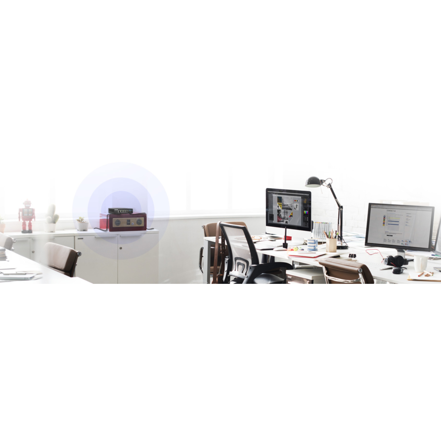 Biuro z dwoma monitorami, biurkiem i czerwonym routerem emitującym sygnał.