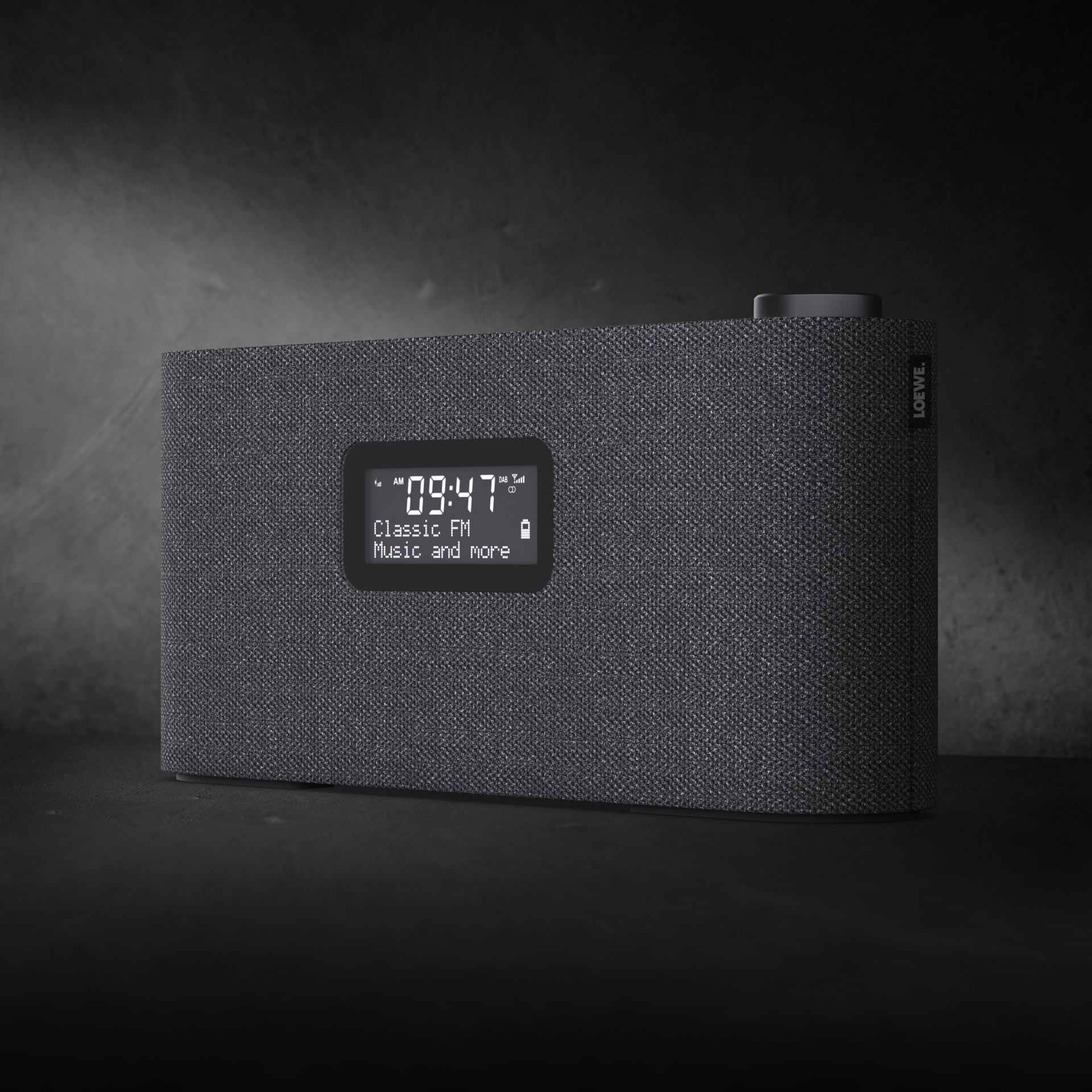 Szary głośnik Loewe wyświetla godzinę i stację radiową na ciemnym tle.
