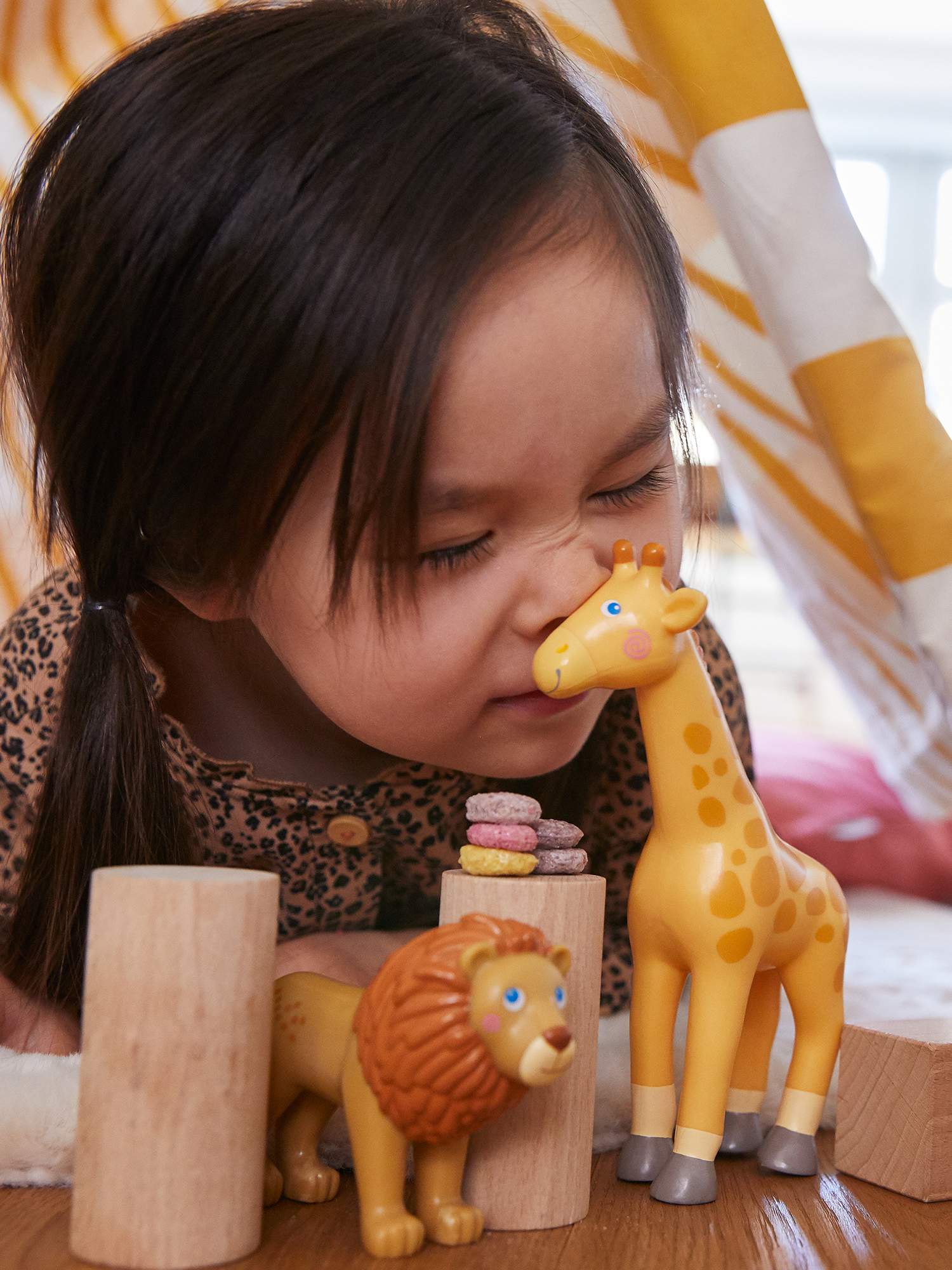 Ein Kind, das an einem Giraffen-Spielzeug riecht, mit einem Löwen-Spielzeug und Blöcken davor.