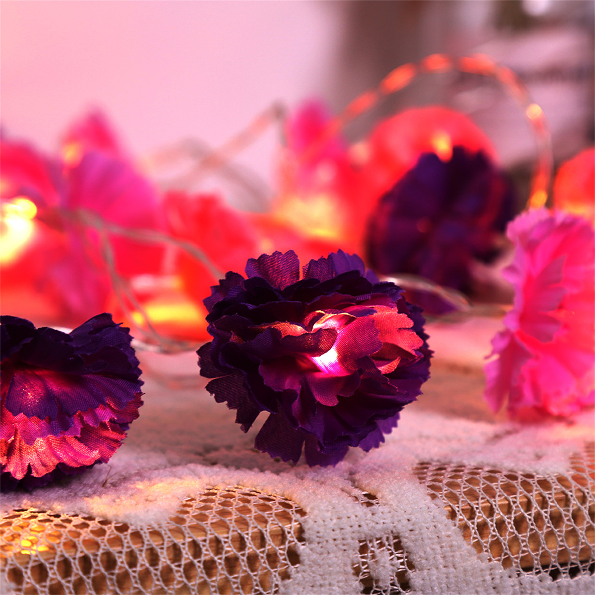 Nahaufnahme von lila Blumen-Lichterketten. Weichzeichner Hintergrund mit mehr Lichtern. Lichter auf einem Tisch.