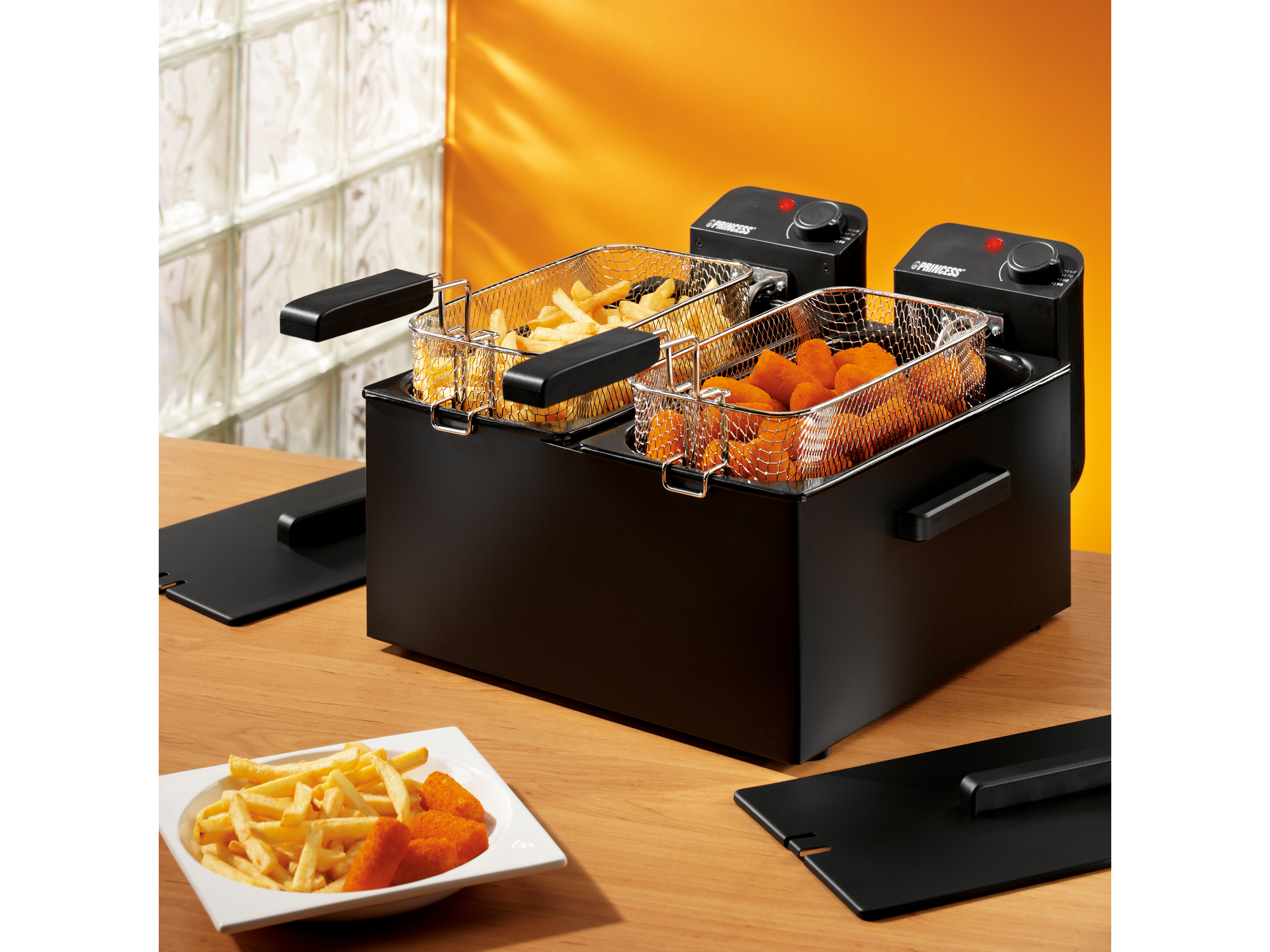 Schwarze Doppel-Fritteuse mit zwei Körben und Essen darin. Oranger Hintergrund.