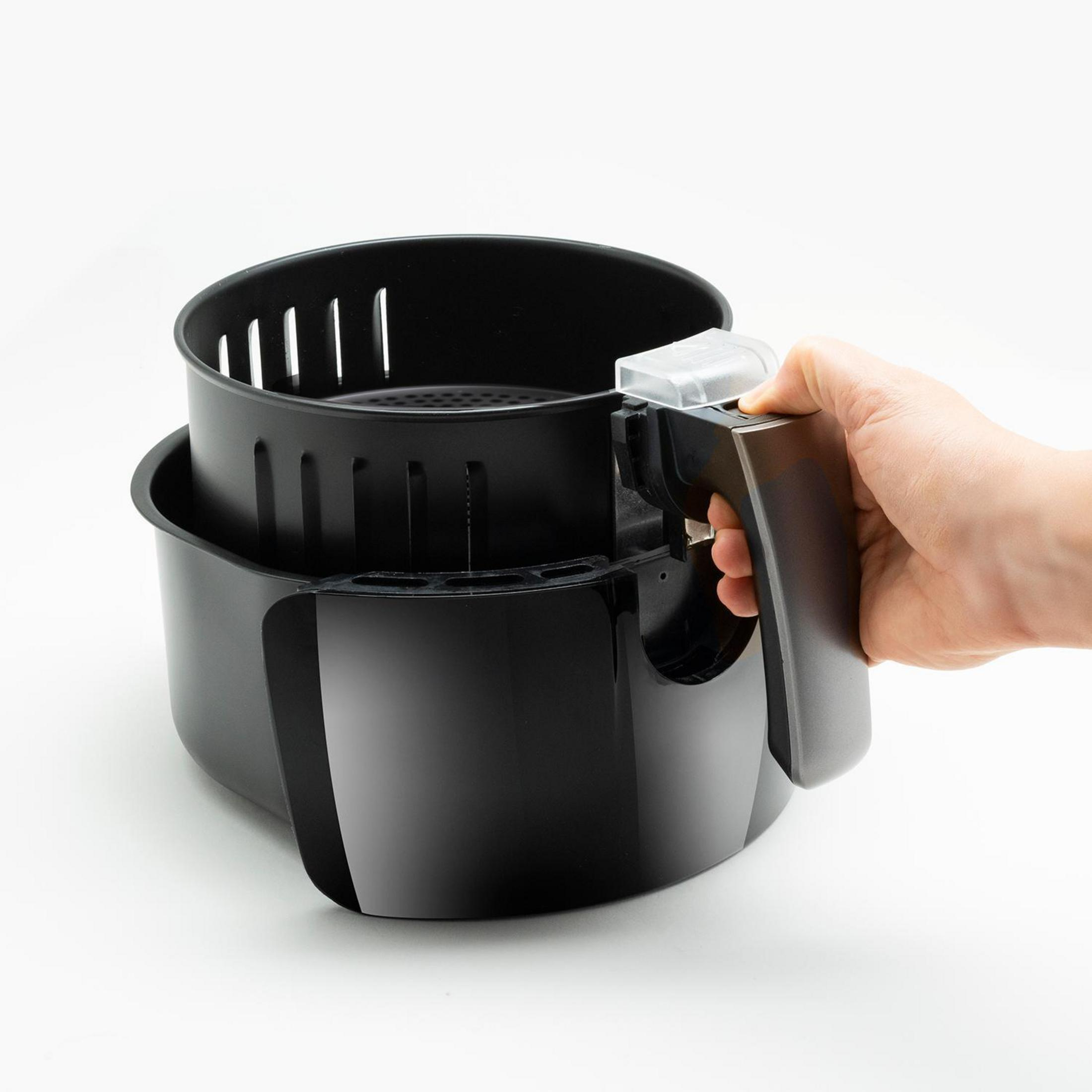 Czarna frytkownica powietrzna z uchwytem. Ręka trzyma uchwyt. Białe tło.
