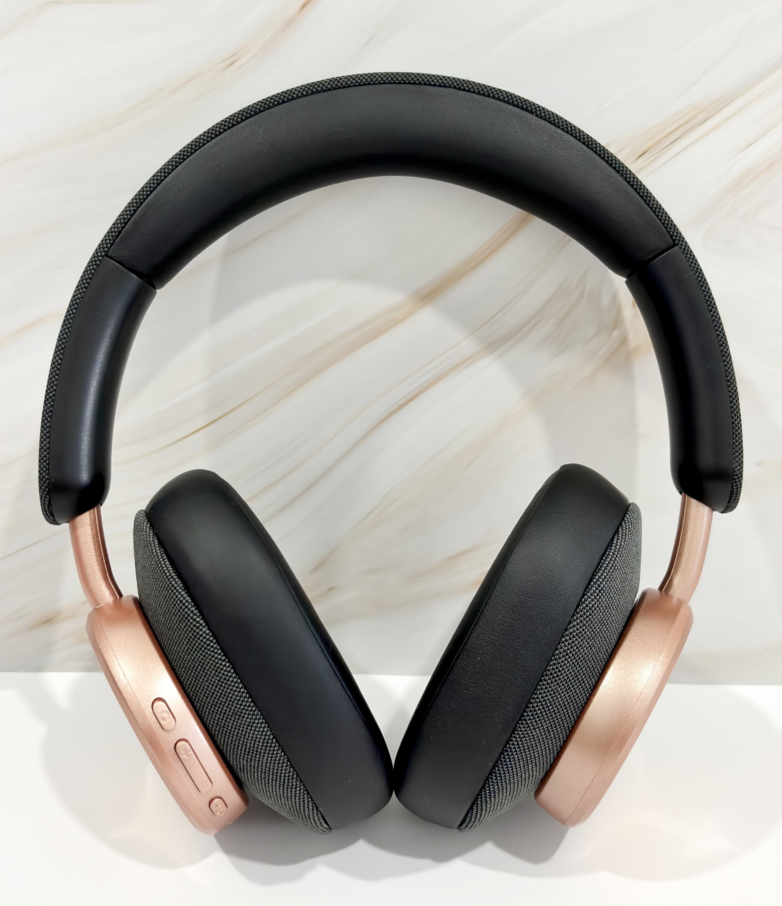 Auriculares, diadema negra, copas rosa oro, sobre superficie de mármol.