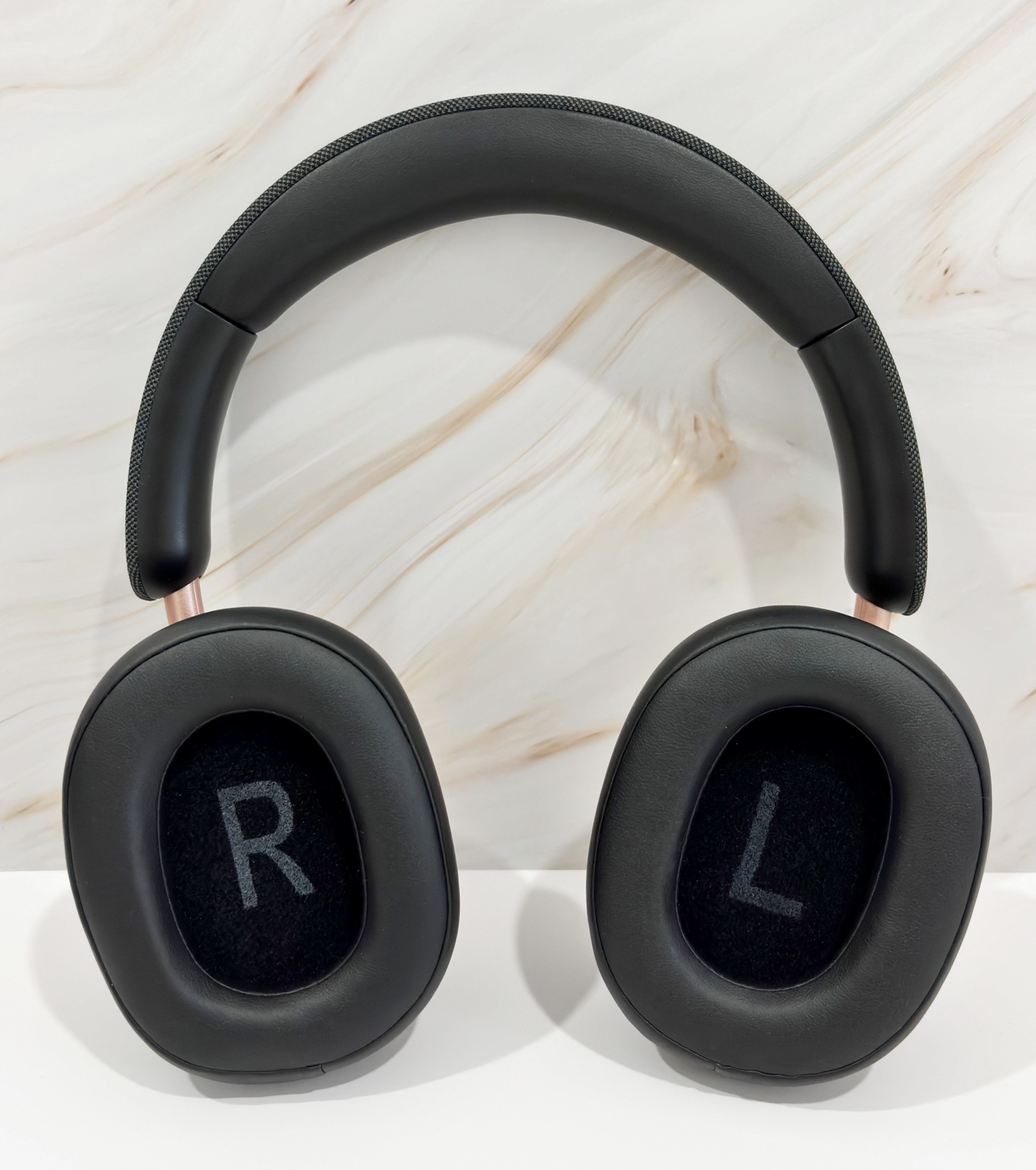 Auriculares negros con detalles en oro rosa sobre superficie blanca. Fondo mármol.
