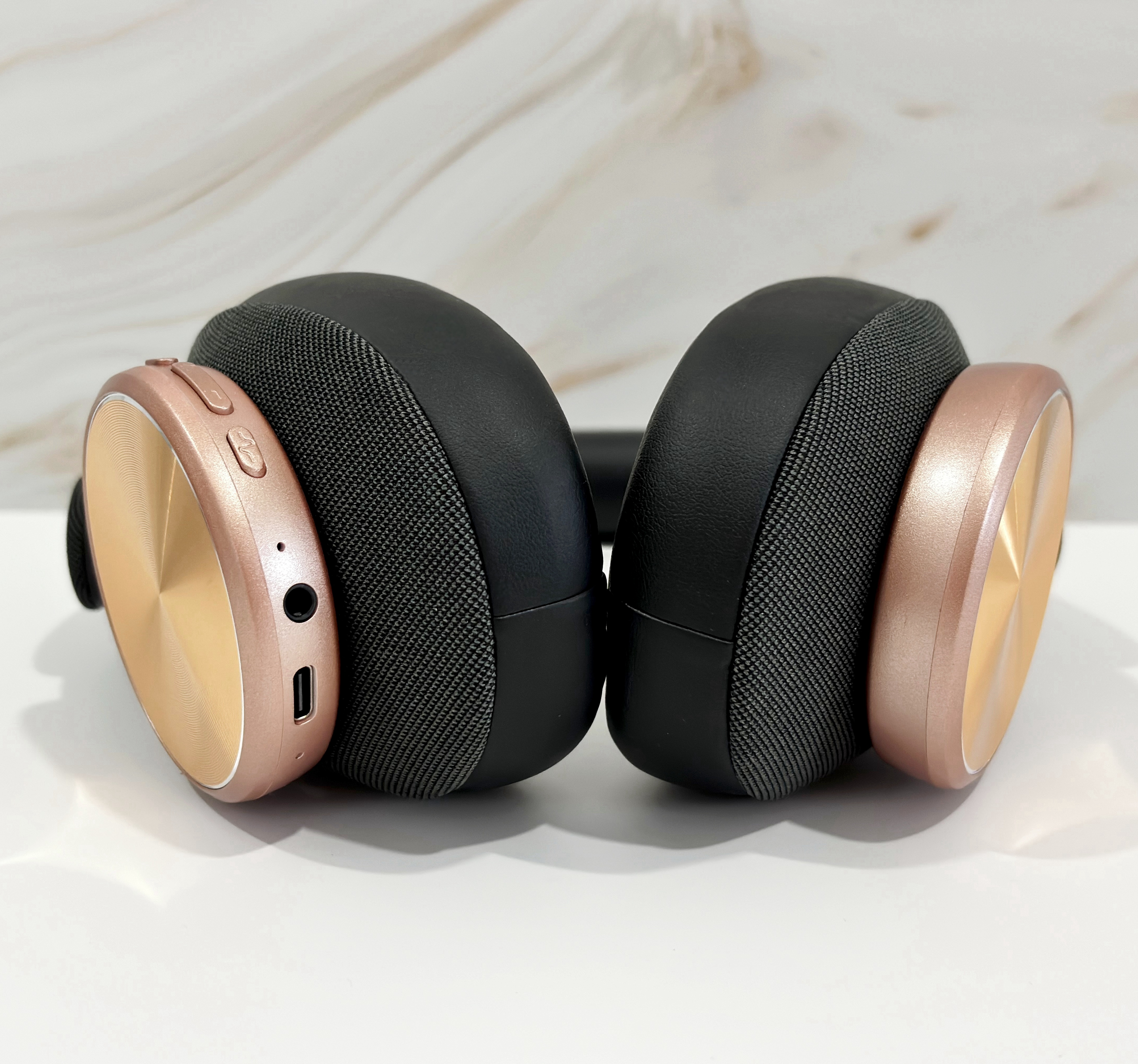 Auriculares negros y oro rosa sobre una superficie blanca.