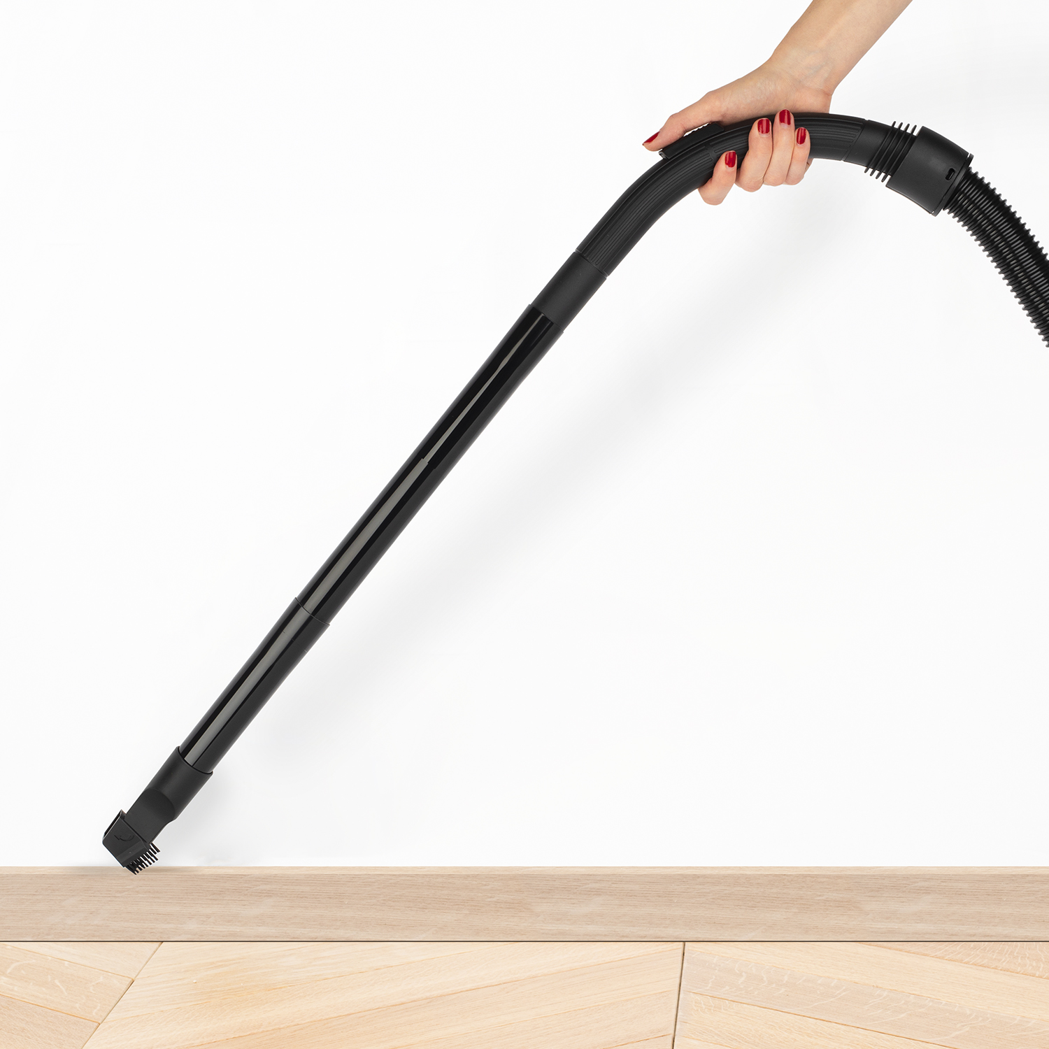 Eine Hand, die einen Staubsaugeraufsatz über einem Holzboden und in der Nähe einer weißen Wand hält.