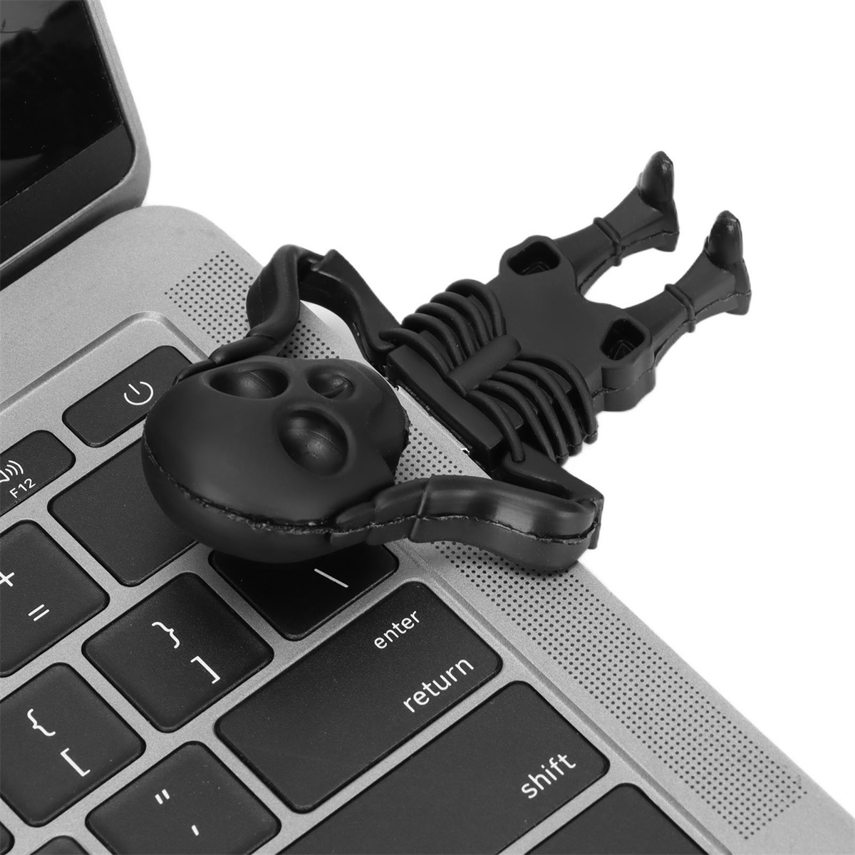 Schwarze Skelettfigur liegt auf einer Laptop-Tastatur. Es ist auf der Ecke des Laptops platziert.