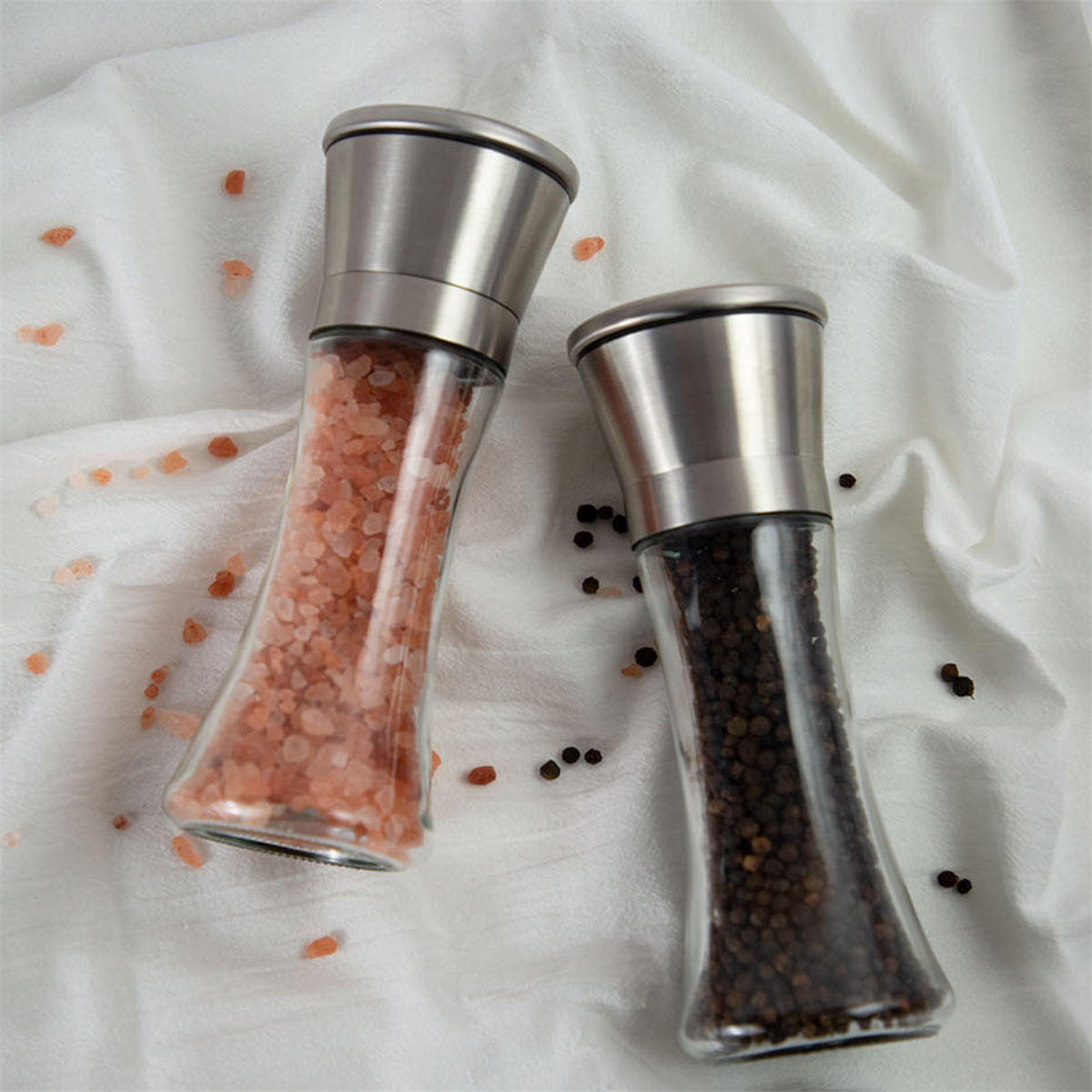Zwei Glas-Salz- und Pfeffermühlen mit Metallaufsätzen, eine rosa, eine schwarz.