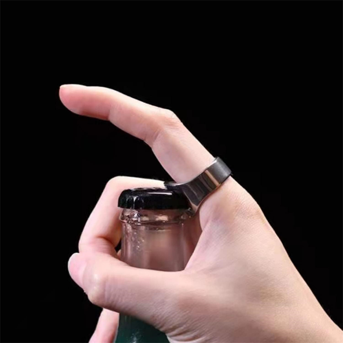 Eine Hand, die einen Ring trägt, der einen Flaschenverschluss öffnet, mit dunklem Hintergrund.