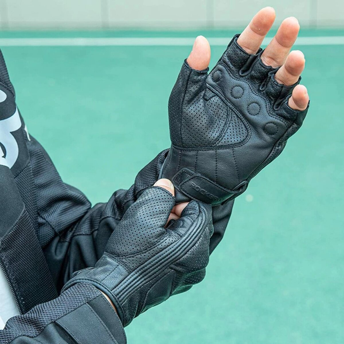 Eine Person trägt schwarze Motorradhandschuhe mit perforiertem Leder und fingerlosem Design.