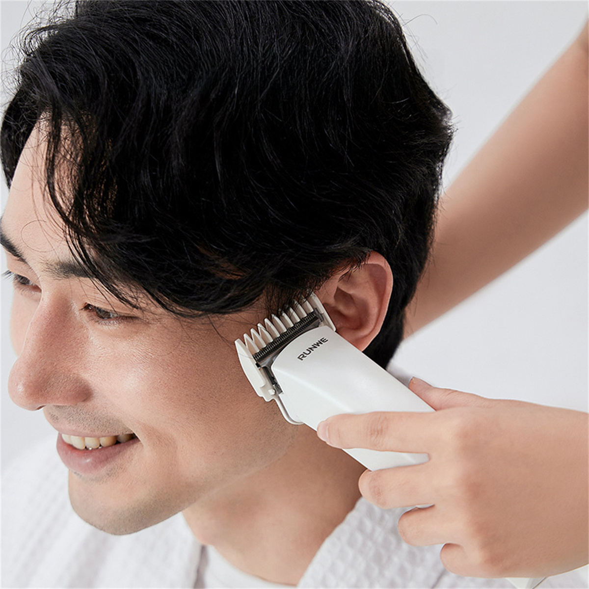 Ein Mann bekommt mit einem weißen Haarschneider die Haare geschnitten.