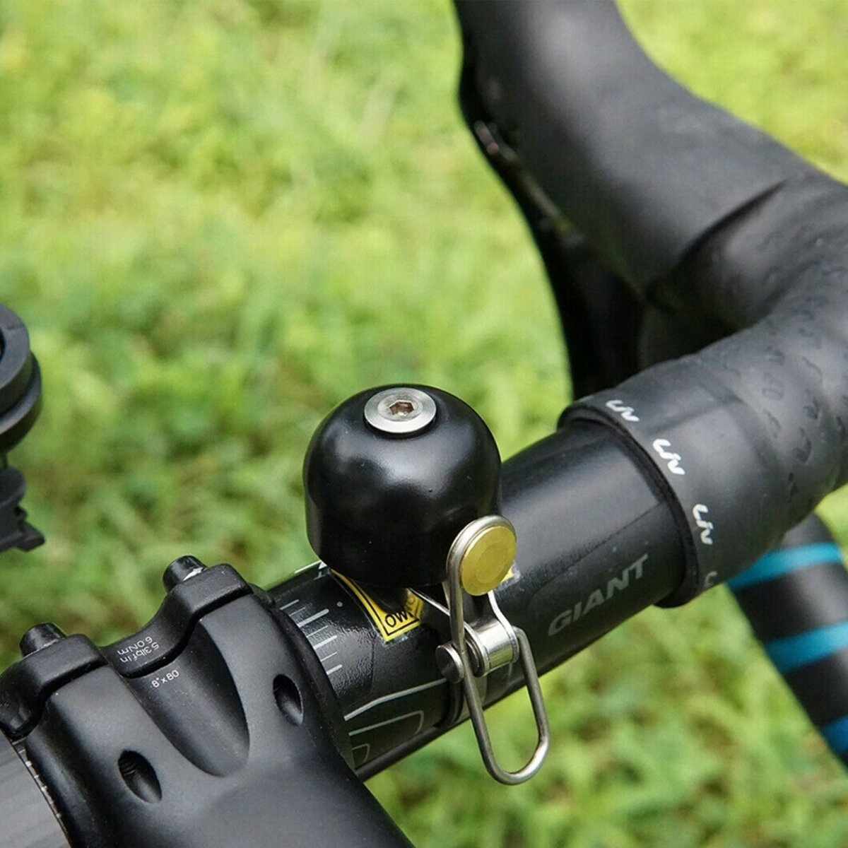 Czarny dzwonek rowerowy na czarnej kierownicy. Zielone tło.