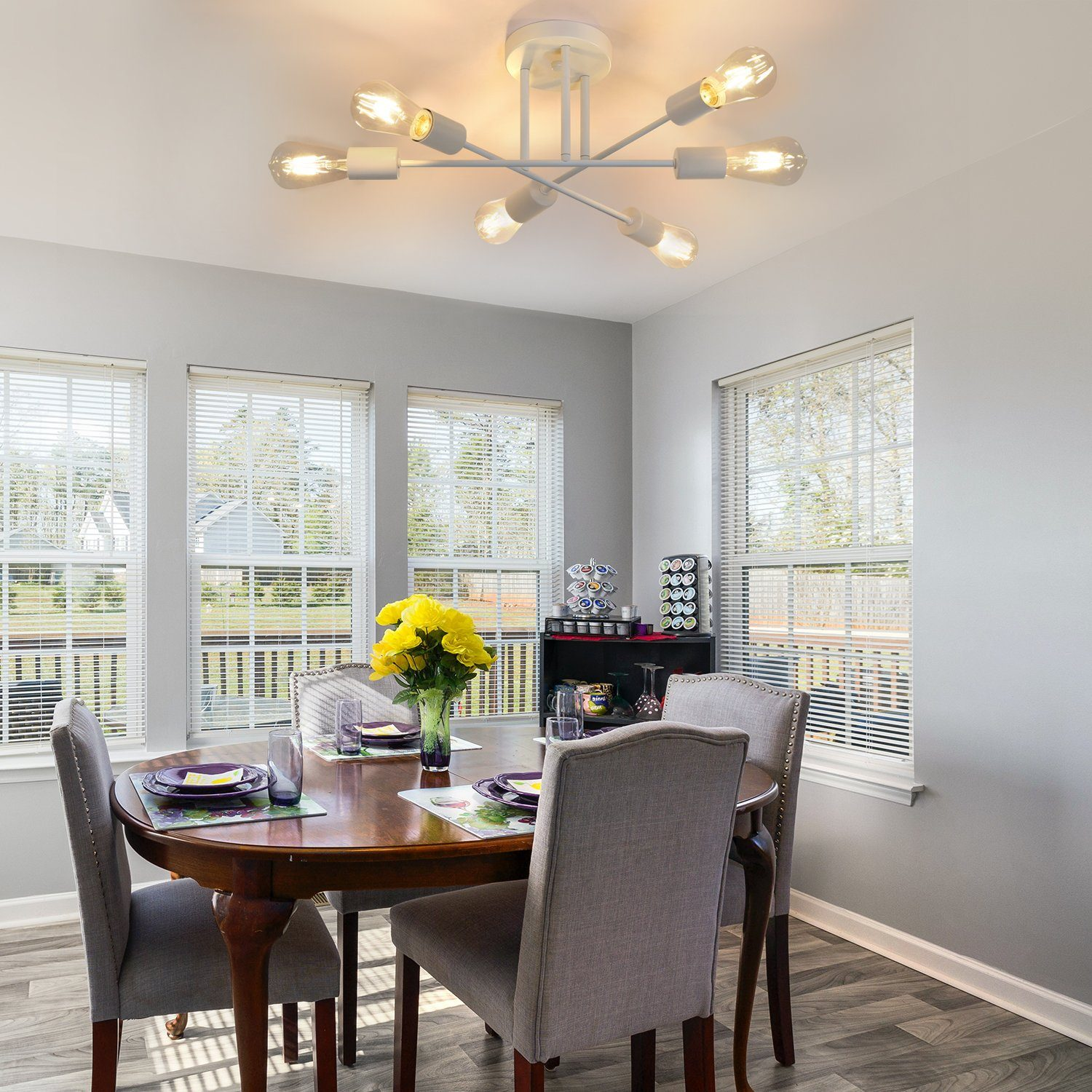 Jadalnia z okrągłym drewnianym stołem i żółtymi kwiatami. Są krzesła i okna.