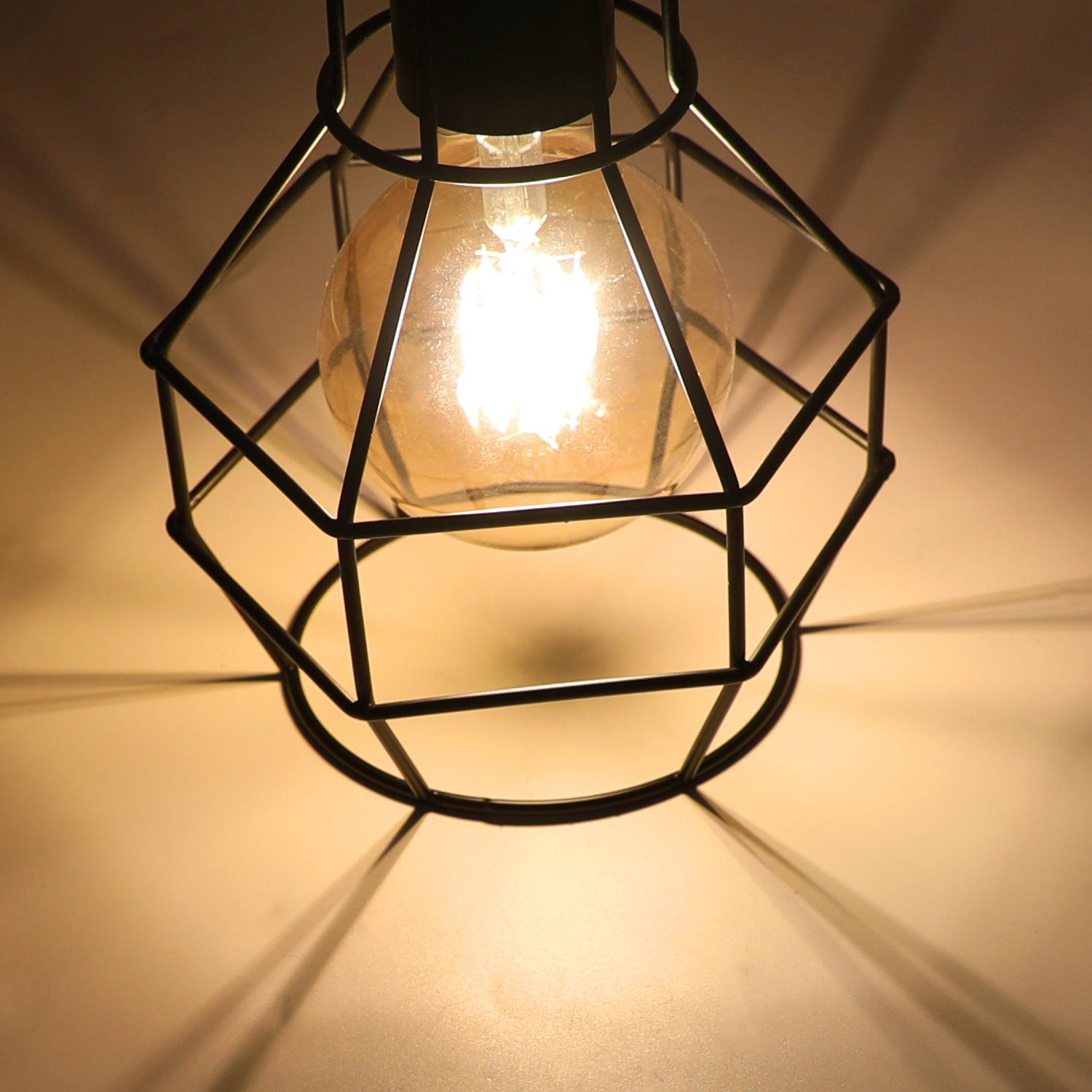 Czarna metalowa lampa w klatce z żarówką w środku. Jasne tło.