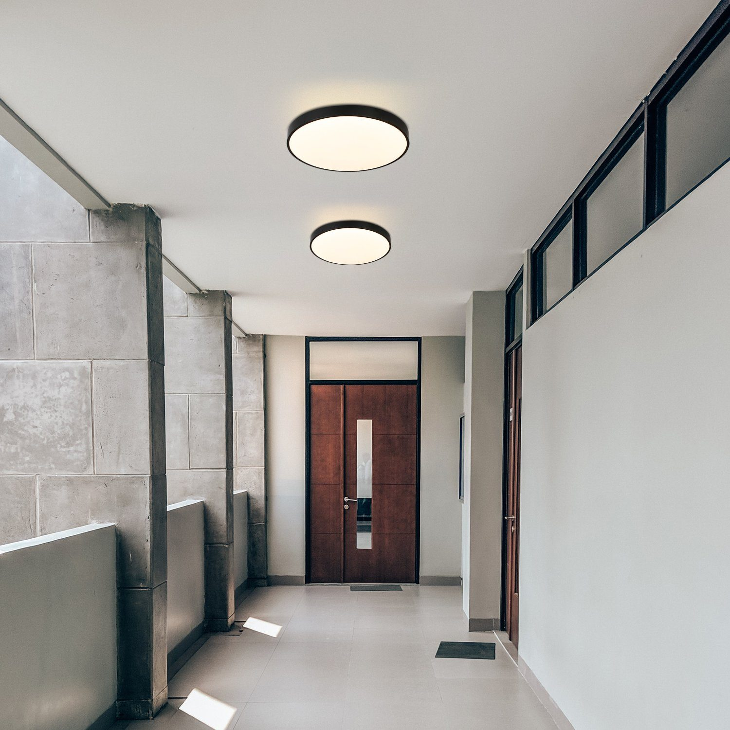Dwa okrągłe światła sufitowe na korytarzu. Drzwi i ściany są jasnego koloru.
