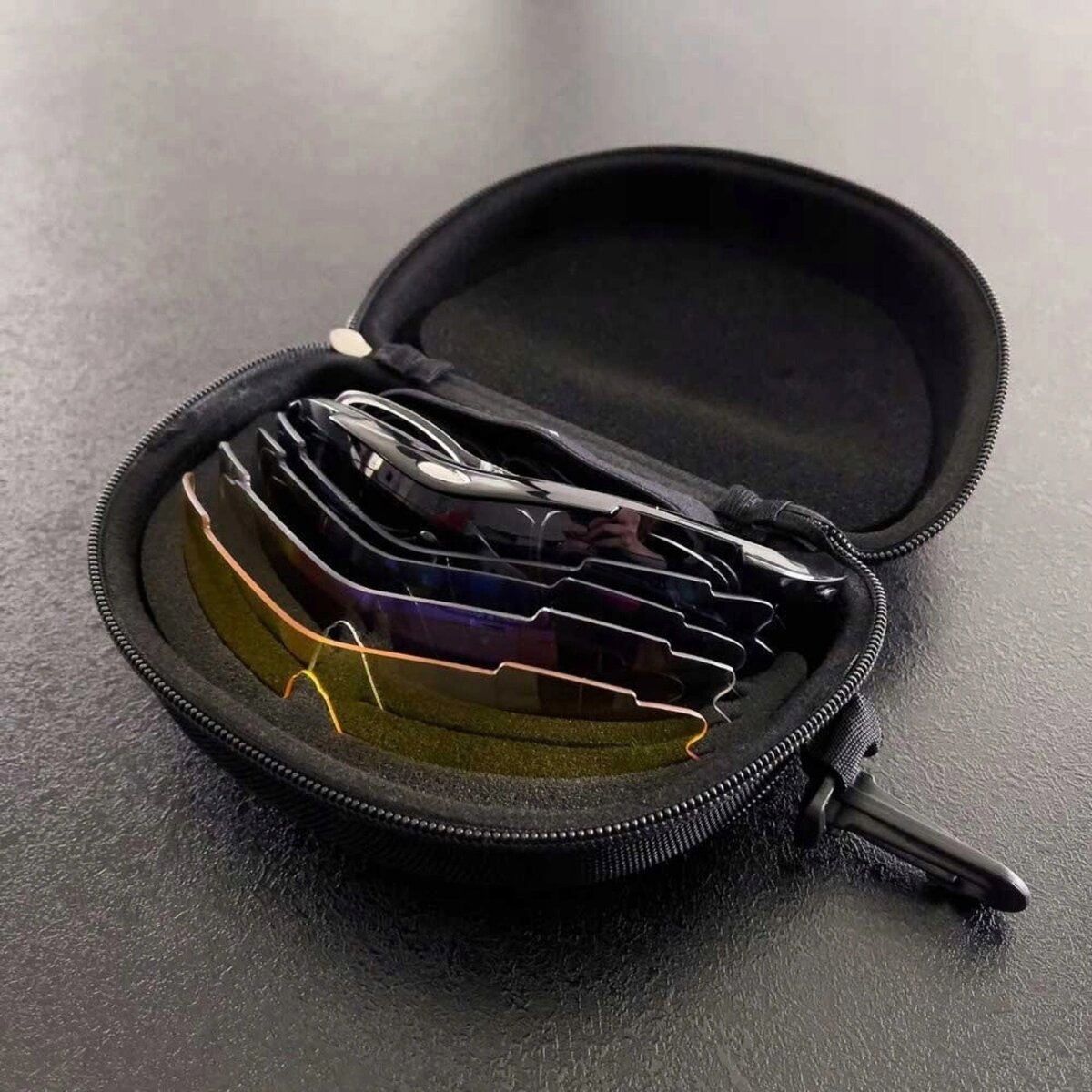 Geöffnete schwarze Reißverschlusstasche mit mehreren Sonnenbrillen. Die Tasche liegt auf dunkler Oberfläche.