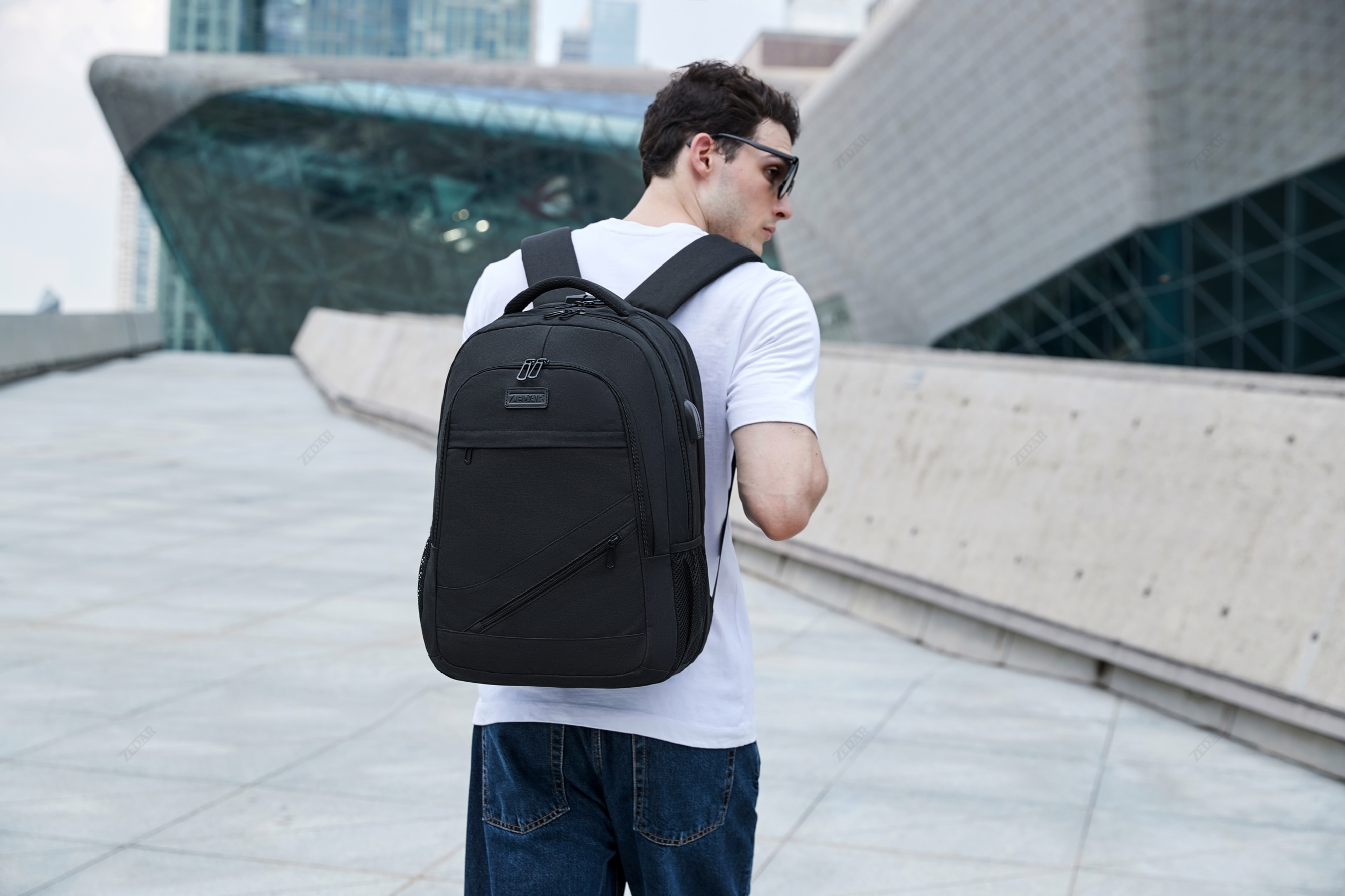 Ein Mann mit Rucksack, der von der Kamera wegsieht, Stadtgebäude im Hintergrund.