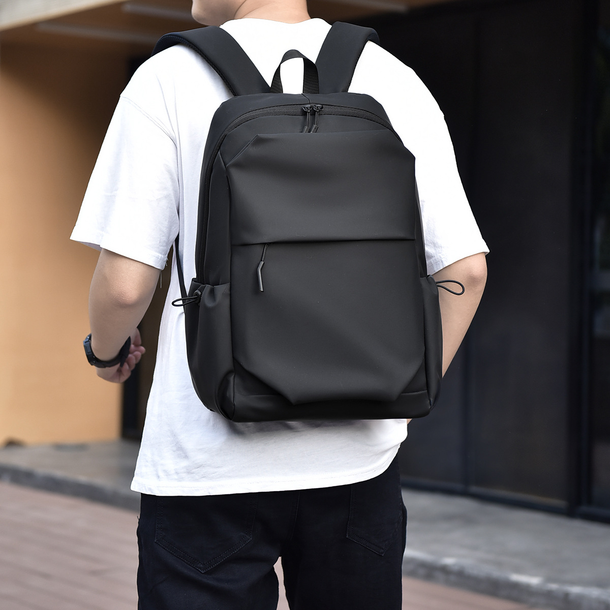 Eine Person trägt einen schwarzen Rucksack mit gepolsterten Trägern, einer Vordertasche und Seitentaschen.