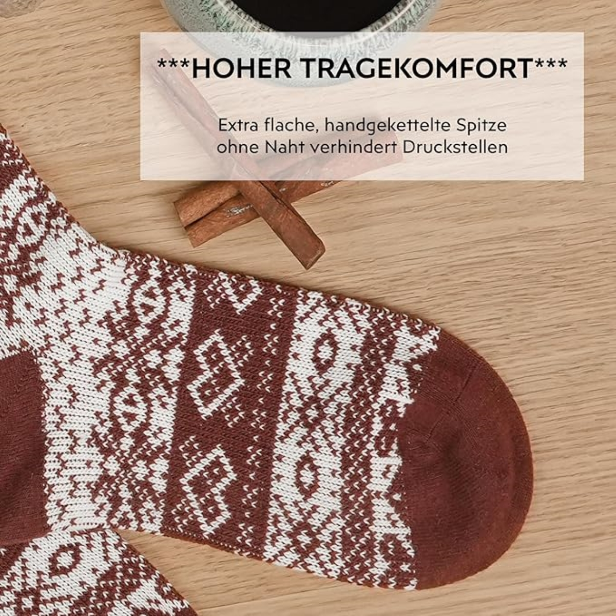 Nahaufnahme einer Socke mit Muster und einem Zimtstangen daneben auf Holzoberfläche.