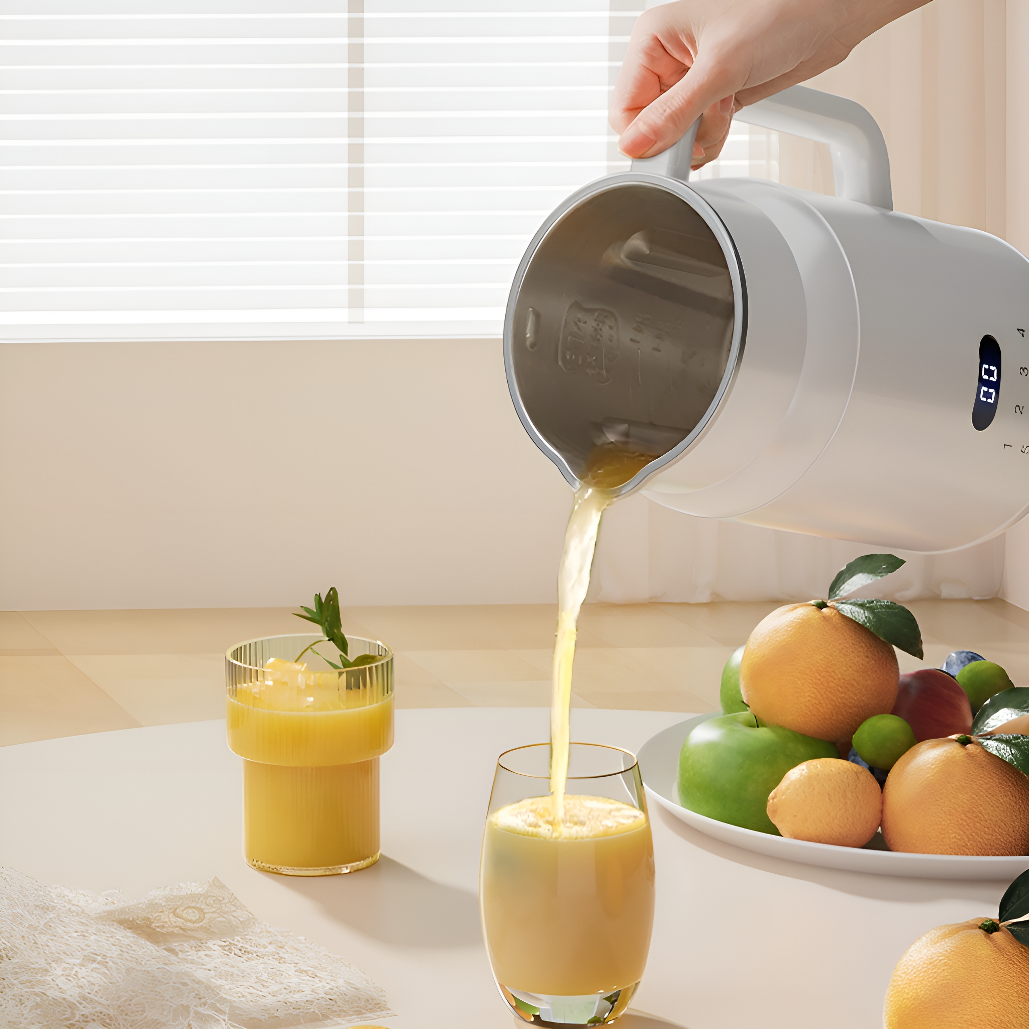 Eine Hand gießt Saft aus einem weißen Mixer in ein Glas. Orangen, Äpfel und Früchte liegen auf einem Teller.