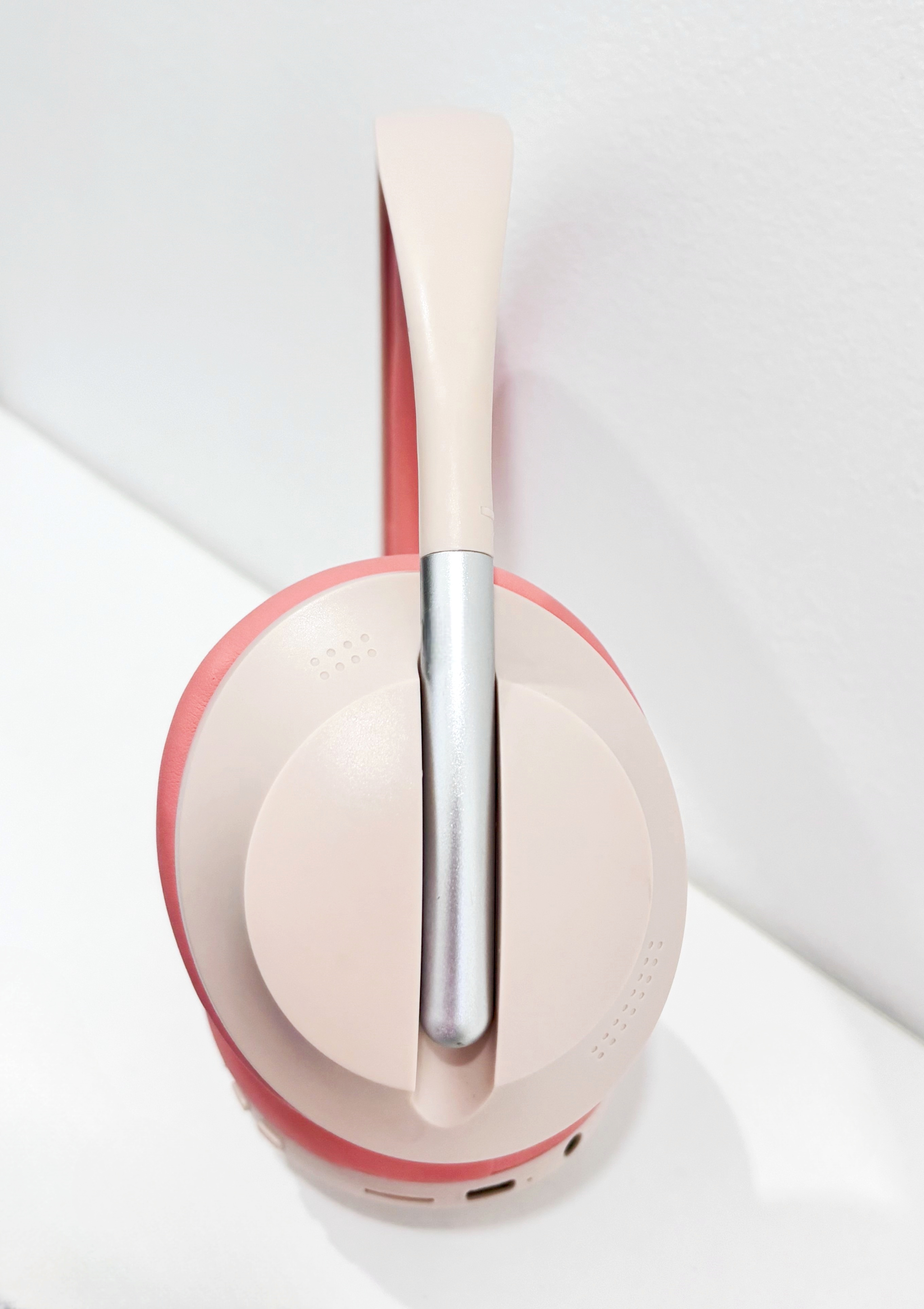 Auriculares rosas y beige, vista lateral, con banda plateada, colocados sobre superficie blanca.
