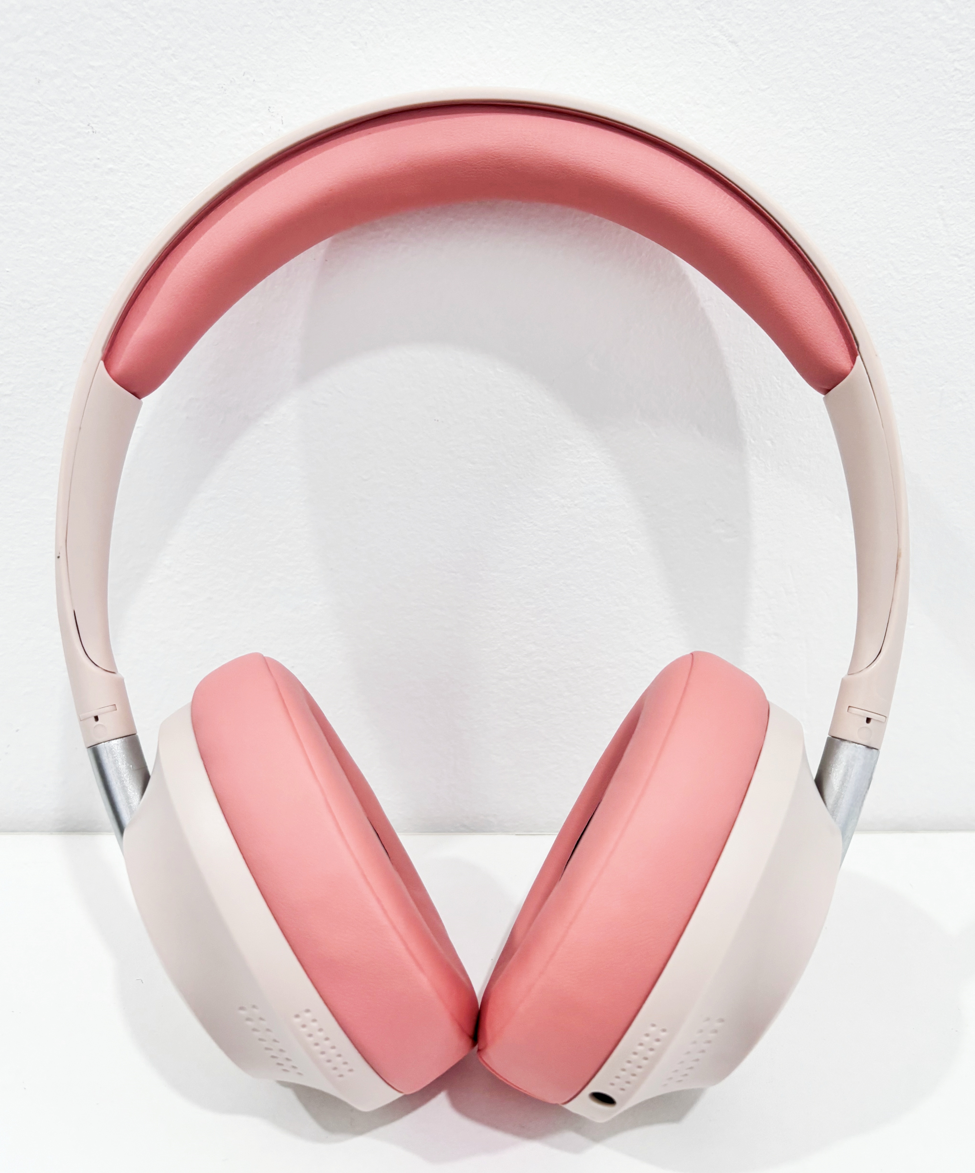 Auriculares rosas y beige sobre superficie blanca, diadema y auriculares rosas.