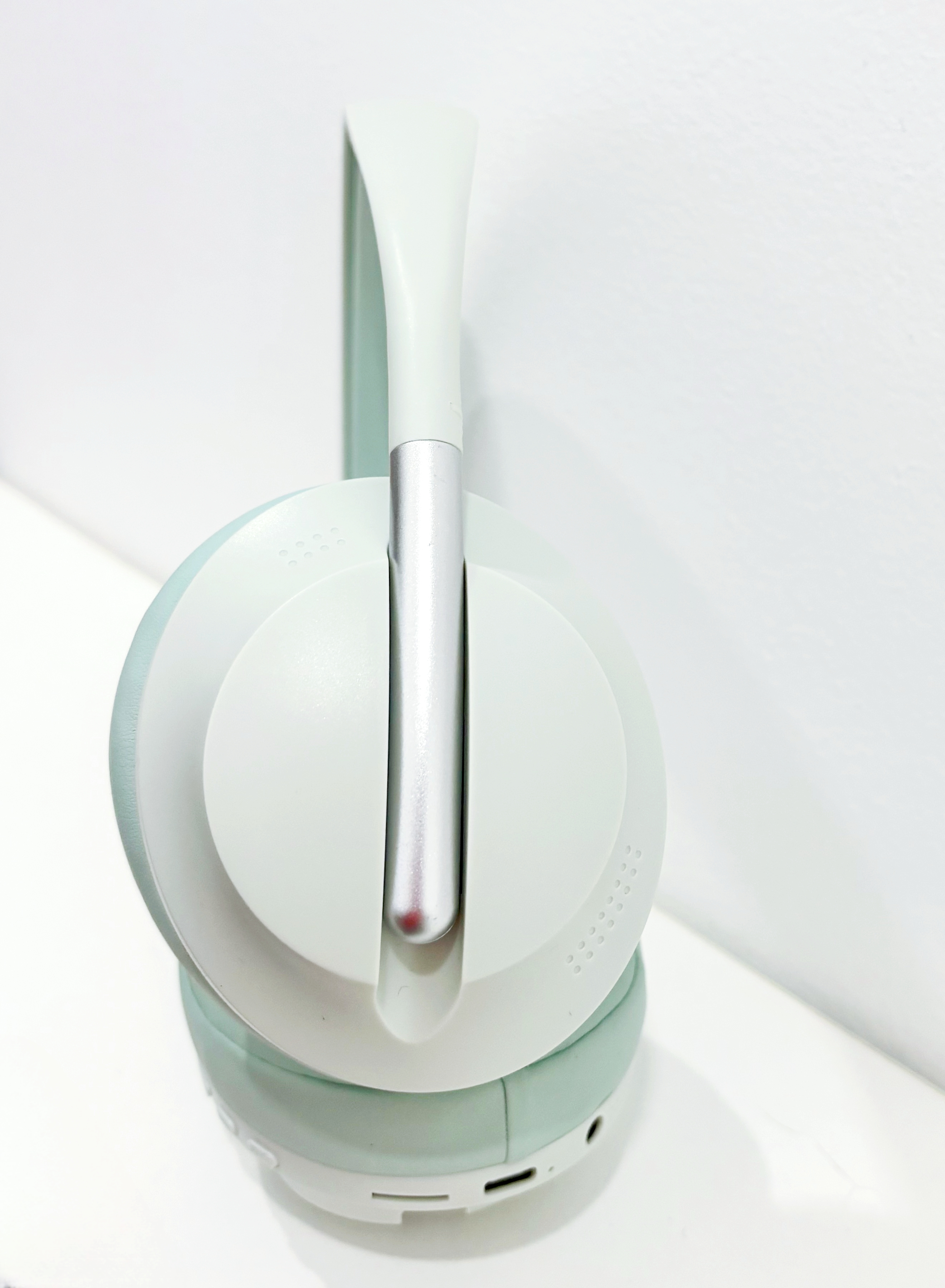 Auriculares, blancos y verde azulado. Brazo plateado. Fondo blanco. Vista en ángulo.