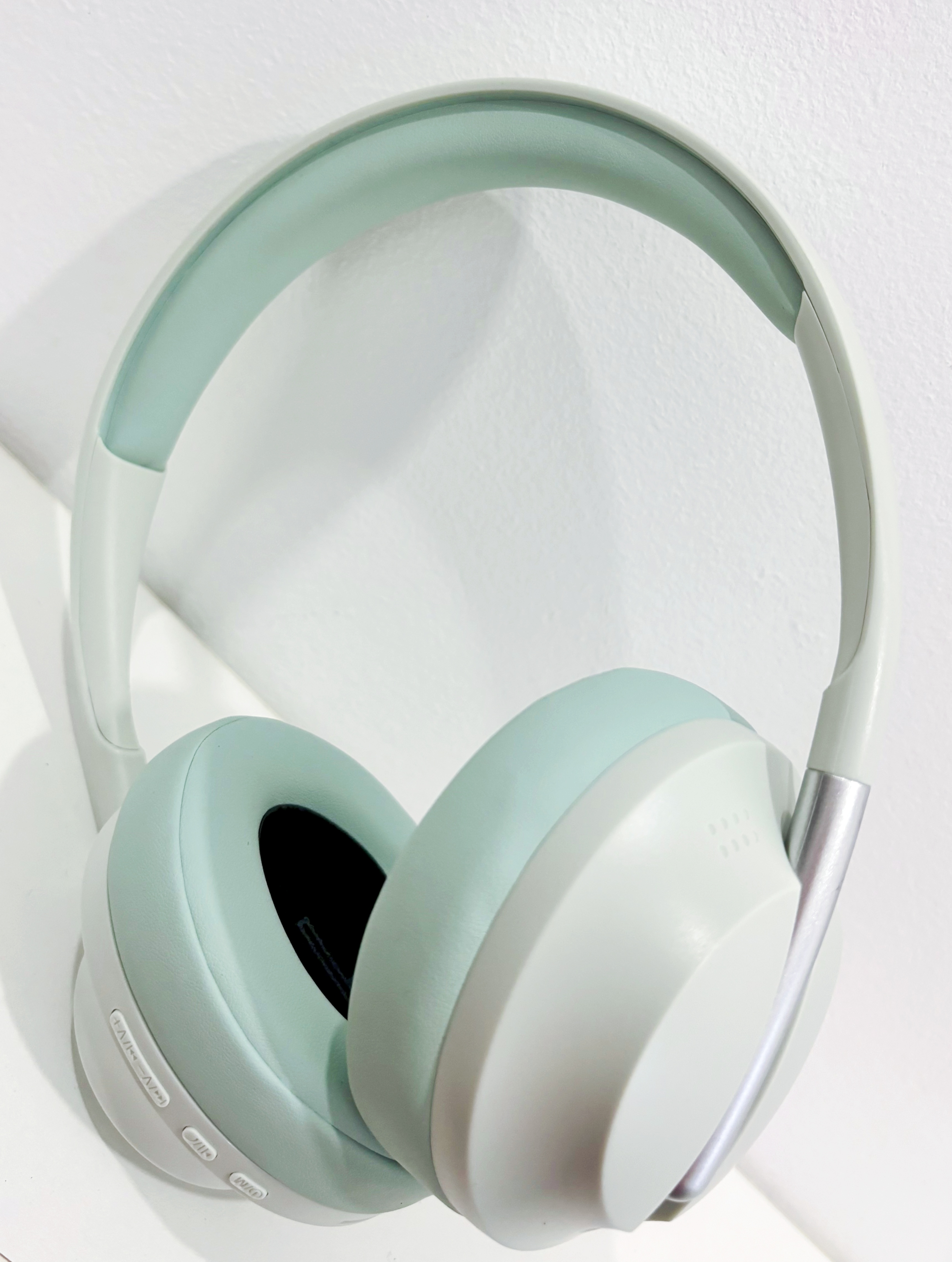 Auriculares con almohadillas y diadema verde claro, detalles plateados. Fondo blanco.