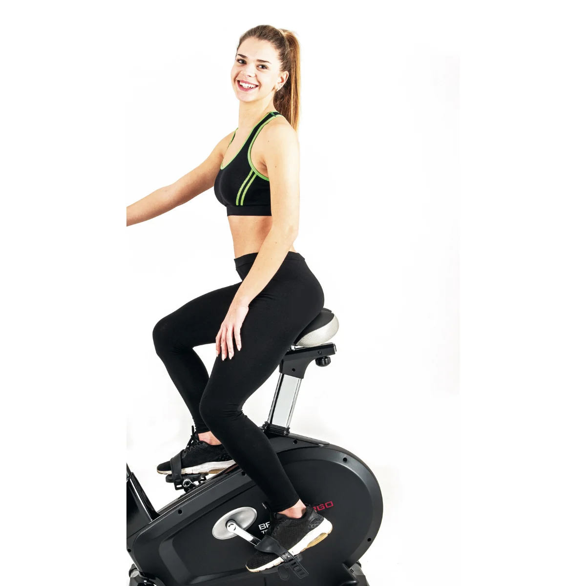 Frau auf dem Heimtrainer. Lächelnde Frau in Sportkleidung, auf einem schwarzen Heimtrainer, weißer Hintergrund.