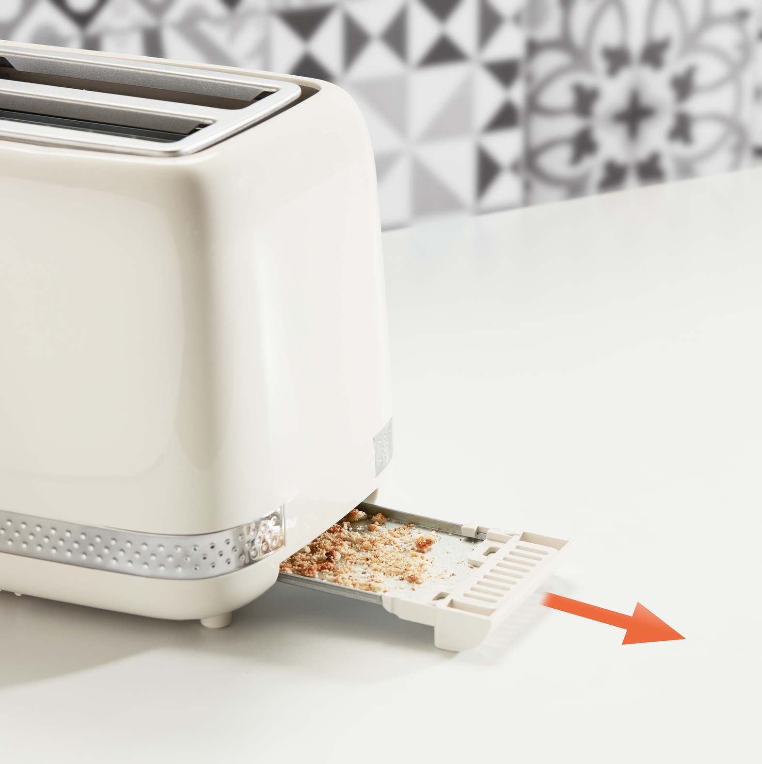 Biały toster z okruchami w tacy i pomarańczową strzałką.