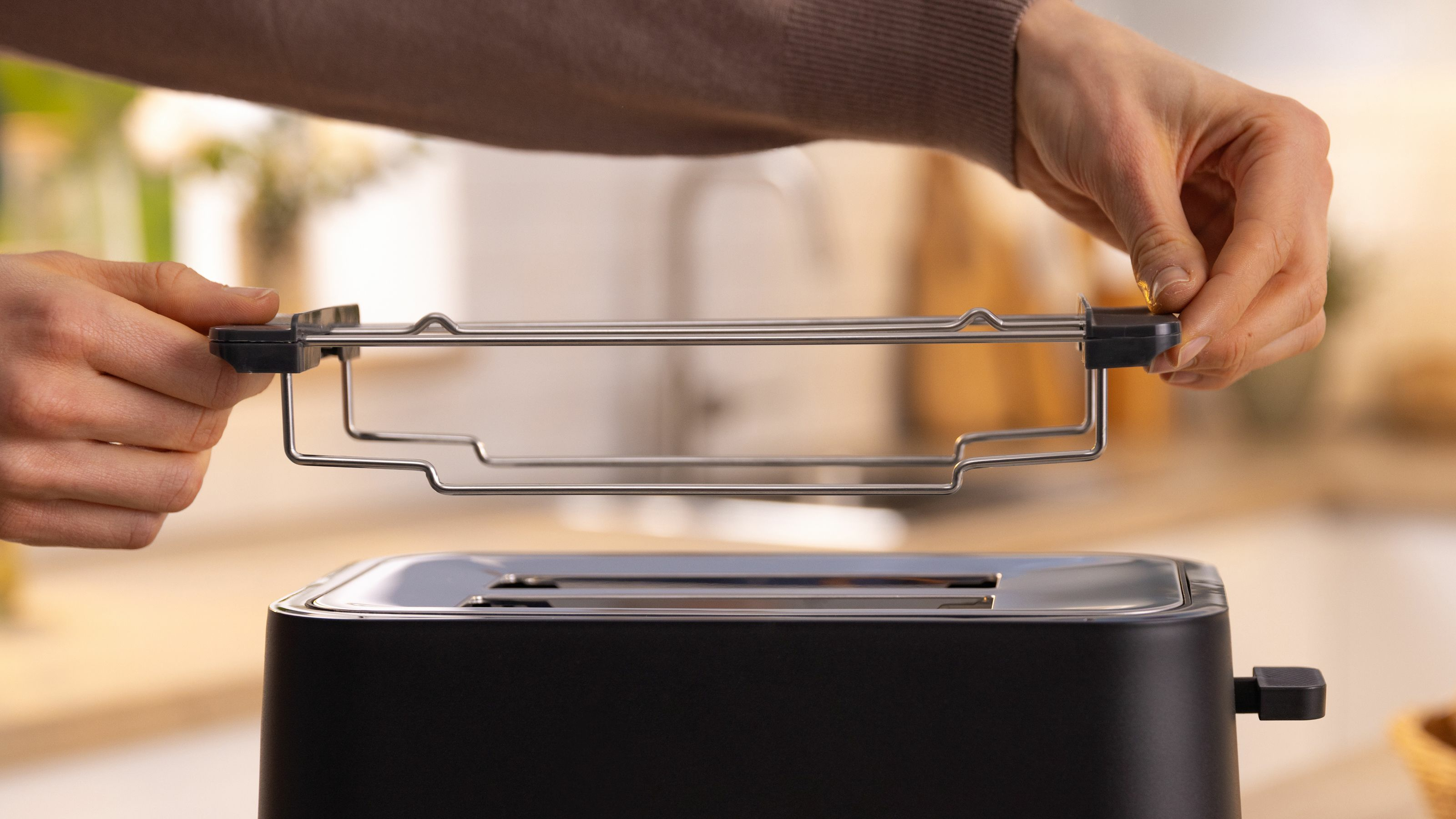Ręka wkładająca ruszt do czarnego tostera. Ostrość na dłoni i tosterze.