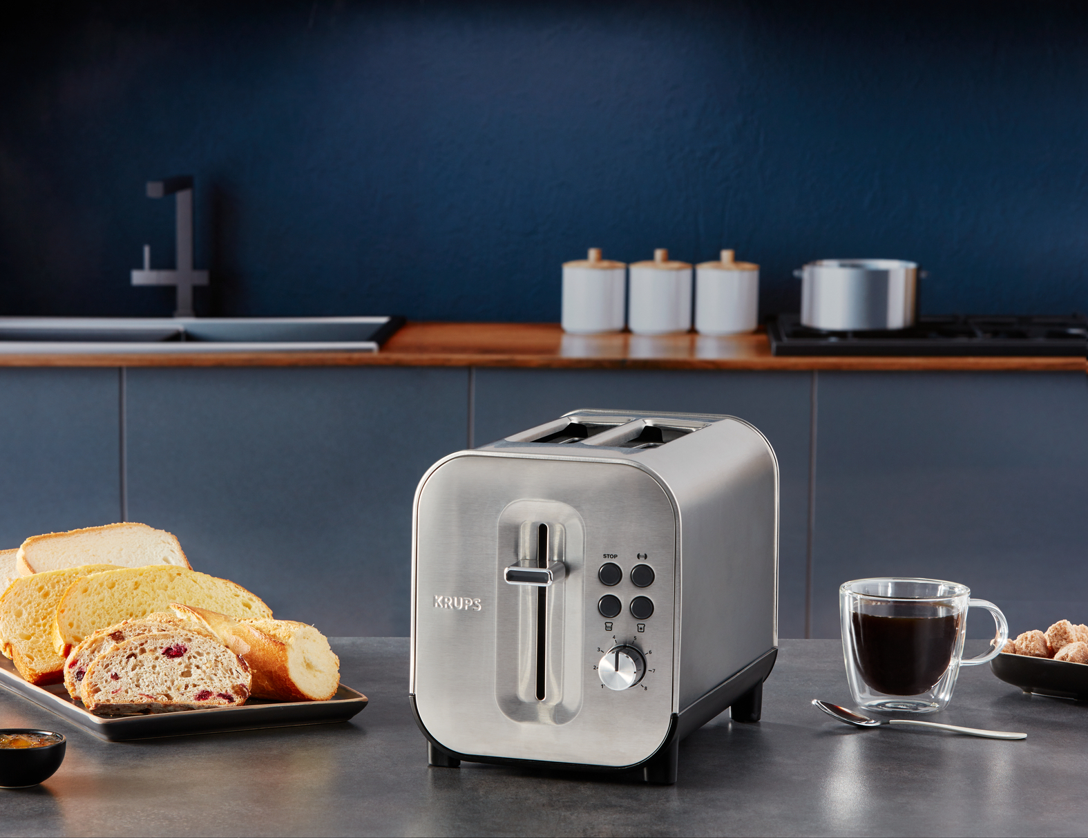 Toster ze stali nierdzewnej z chlebem i filiżanką kawy na szarym blacie.