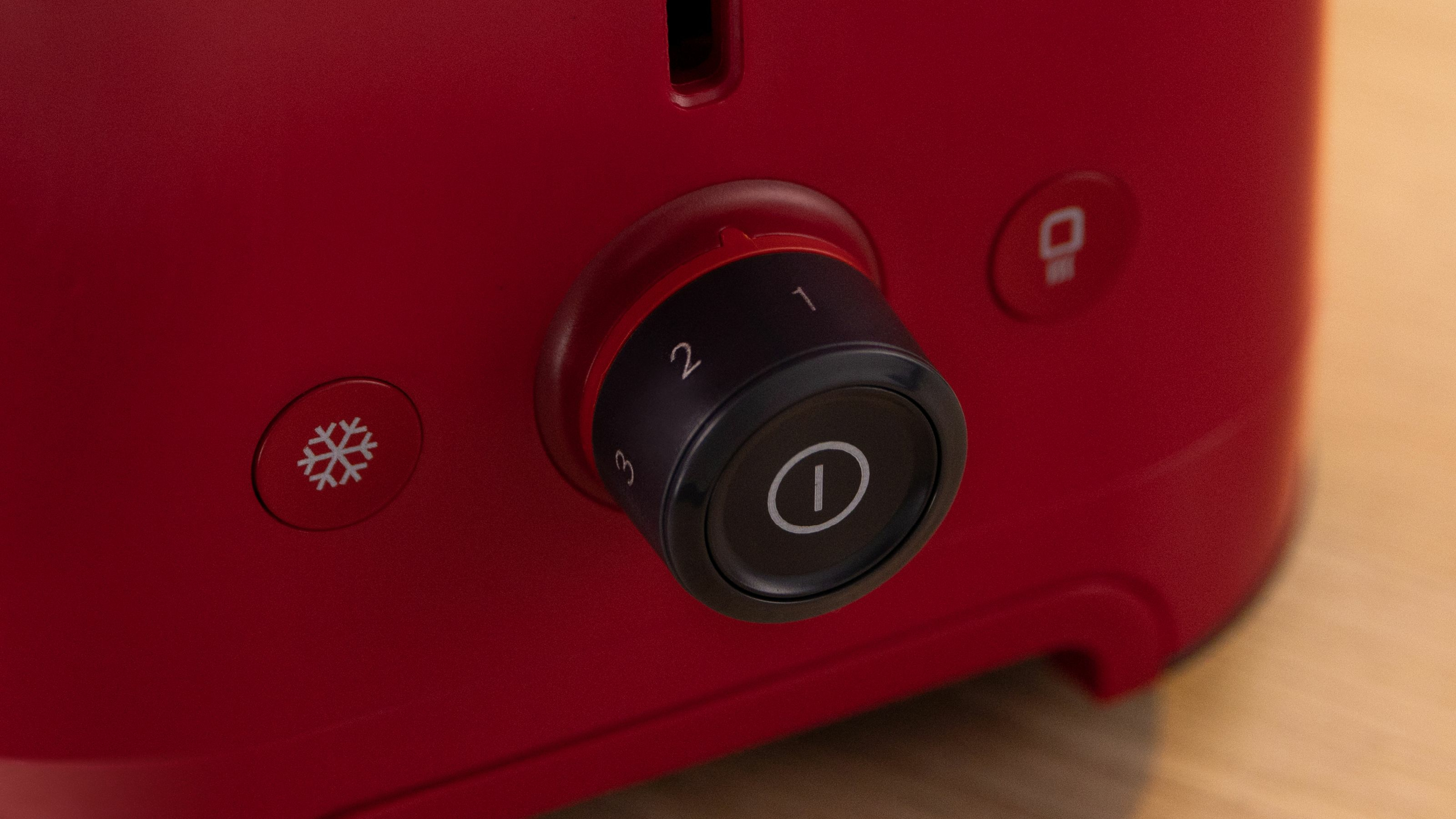 Czerwony toster z czarnym pokrętłem (1-3) i ikonami.